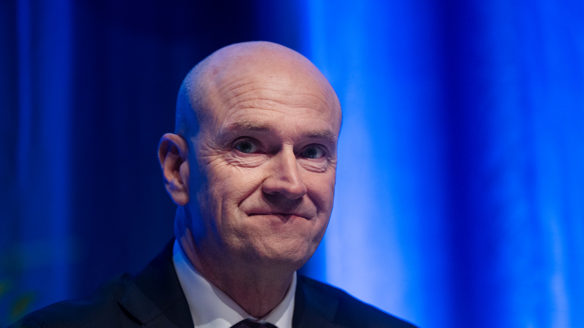 En man i kostym och slips framför en blå bakgrund