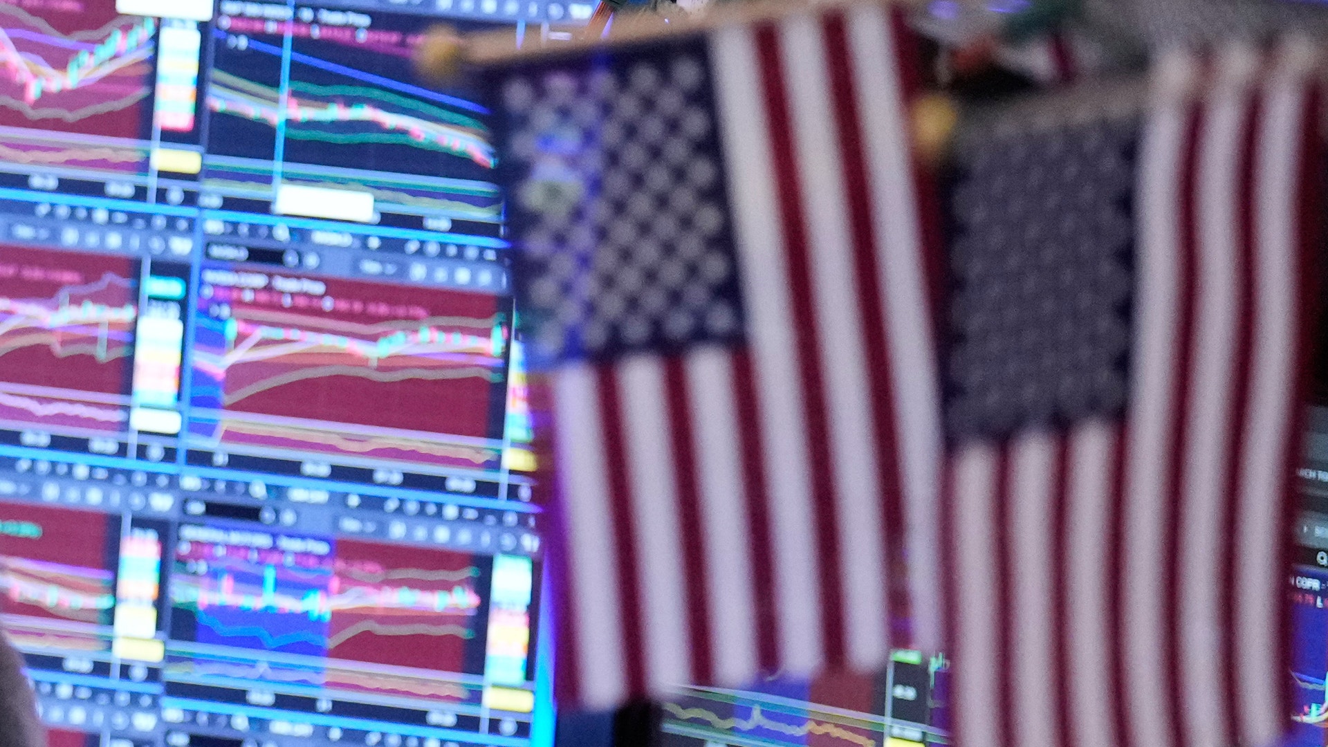 Handelsplats på börsen med datorskärmar som visar marknadsdata och amerikanska flaggor i bakgrunden.
