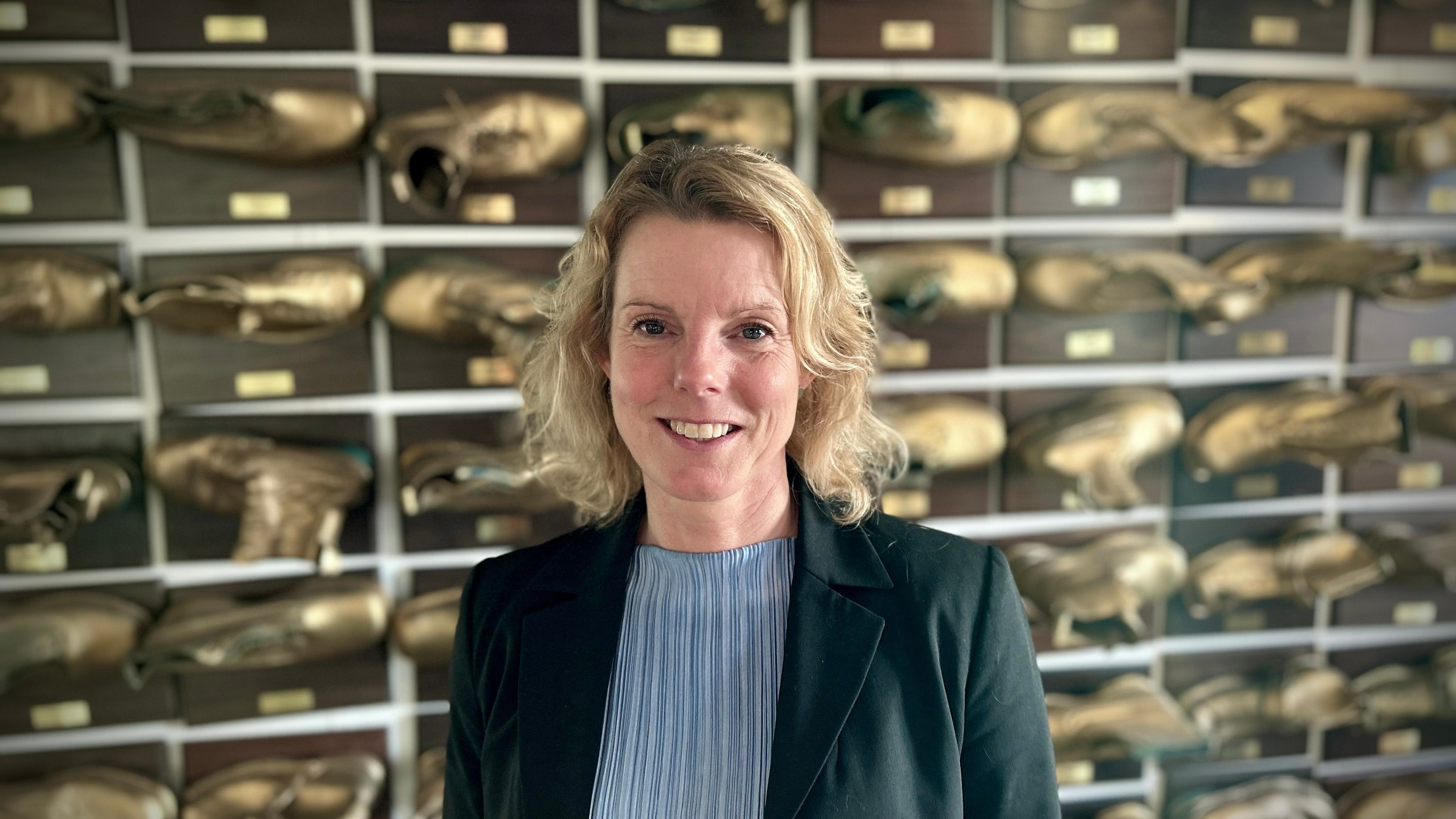 Porträtt av en leende kvinna i mörk kavaj framför en vägg med hyllor