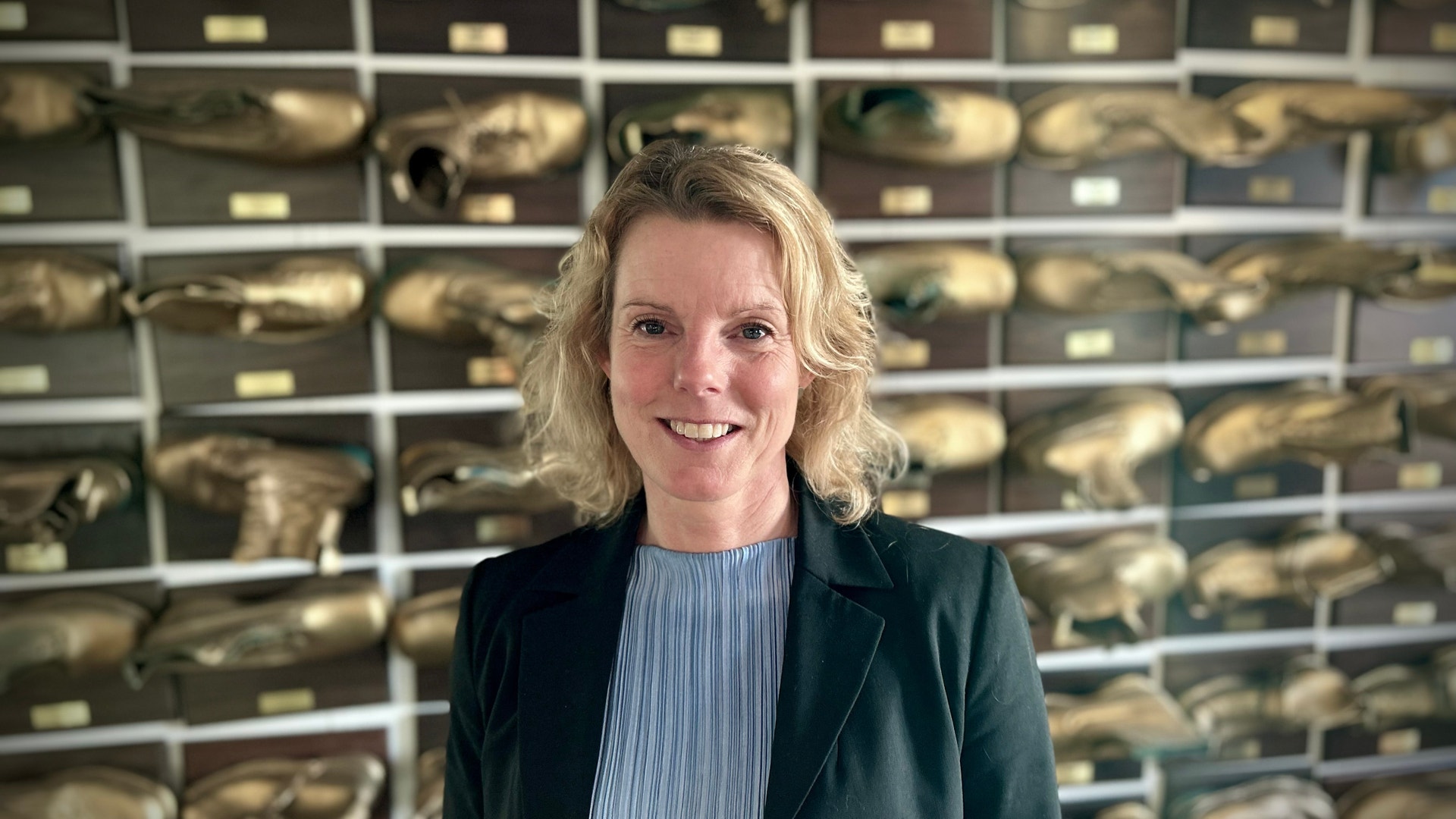 Porträtt av en leende kvinna i mörk kavaj framför en vägg med hyllor