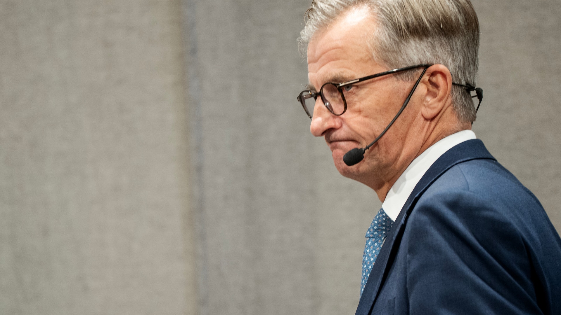 Man i mörk kostym med headset-mikrofon, fotograferad i profil under en presentation eller föreläsning.