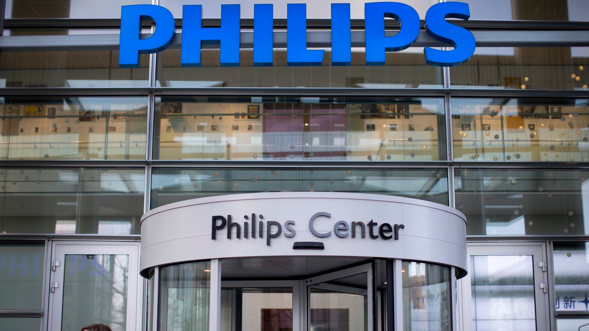Fasaden på Philips Center med blå Philips-logotyp på taket och en rund glassad entrédörr. En person i svart jacka står framför byggnaden.