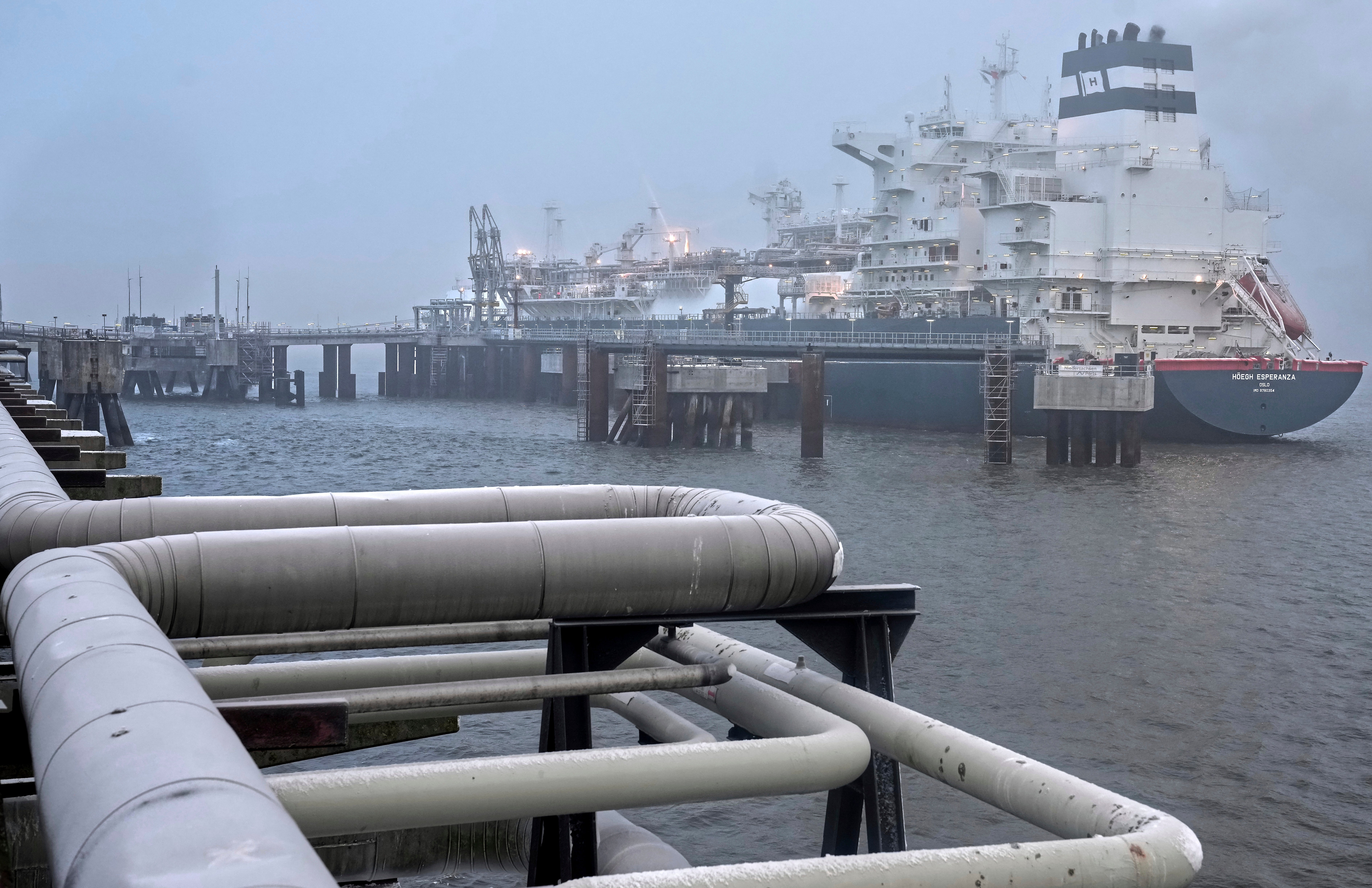 Ett stort industrifartyg dockat vid en hamn med vita rör i förgrunden.