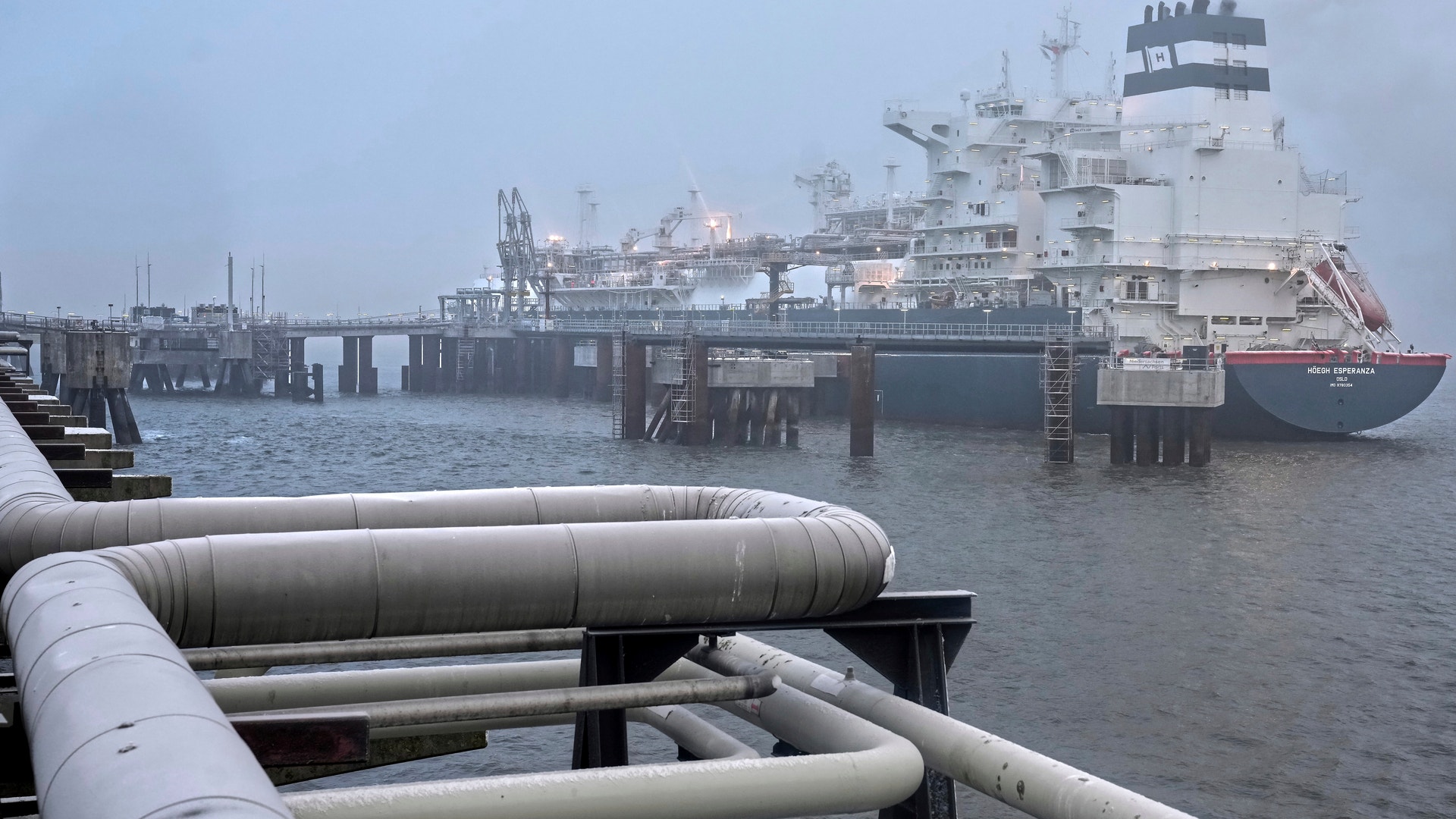 Ett stort industrifartyg dockat vid en hamn med vita rör i förgrunden.