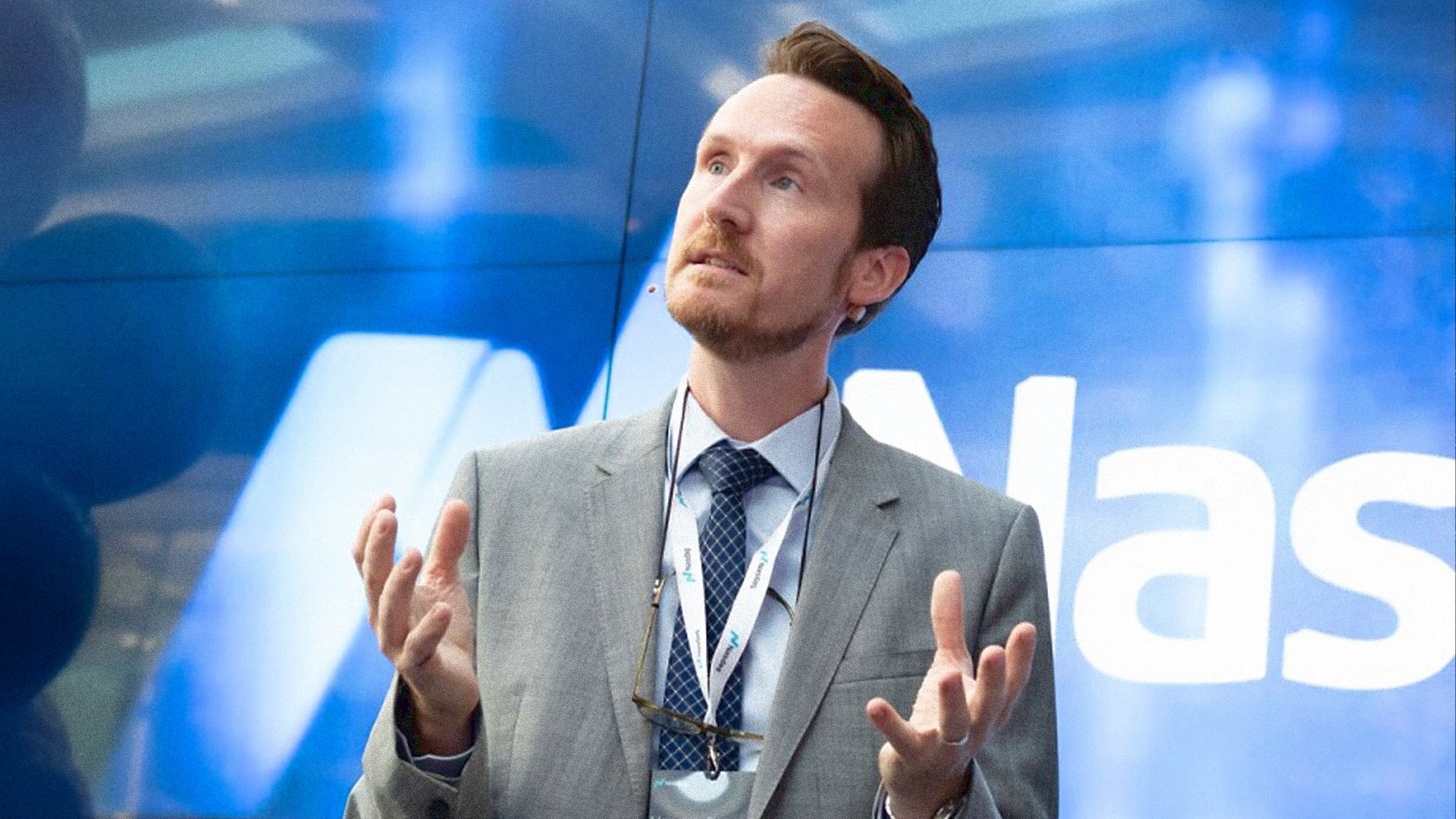 Man i grå kostym ger en presentation på en konferens med blå bakgrund.