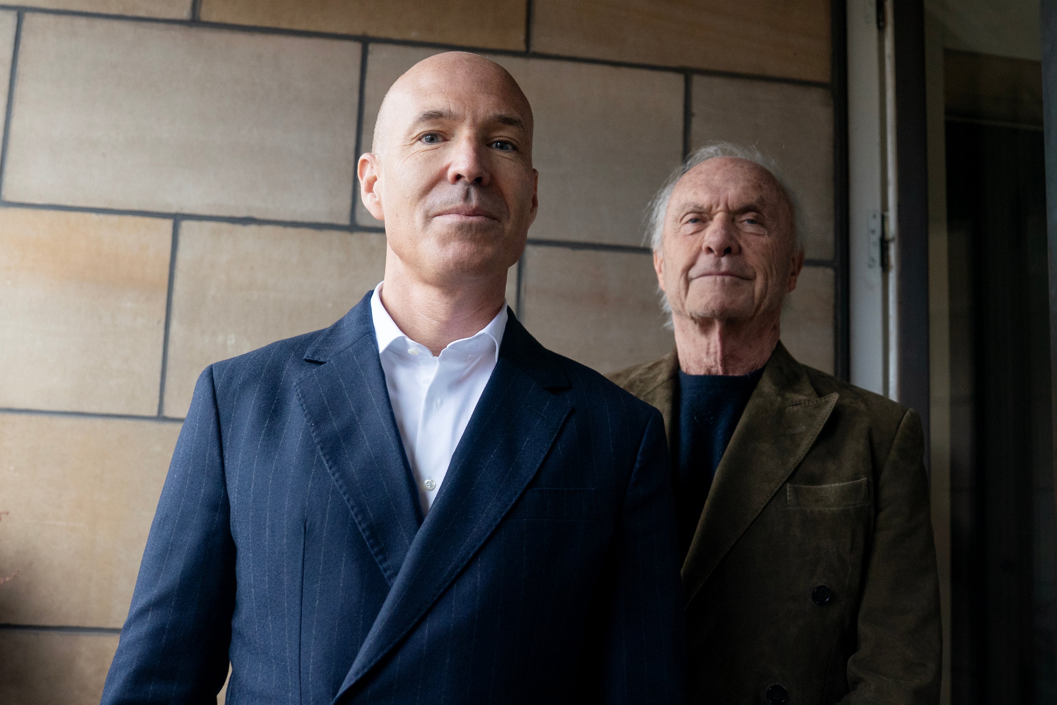 Två män står tillsammans framför en vägg med moderna kakelplattor.