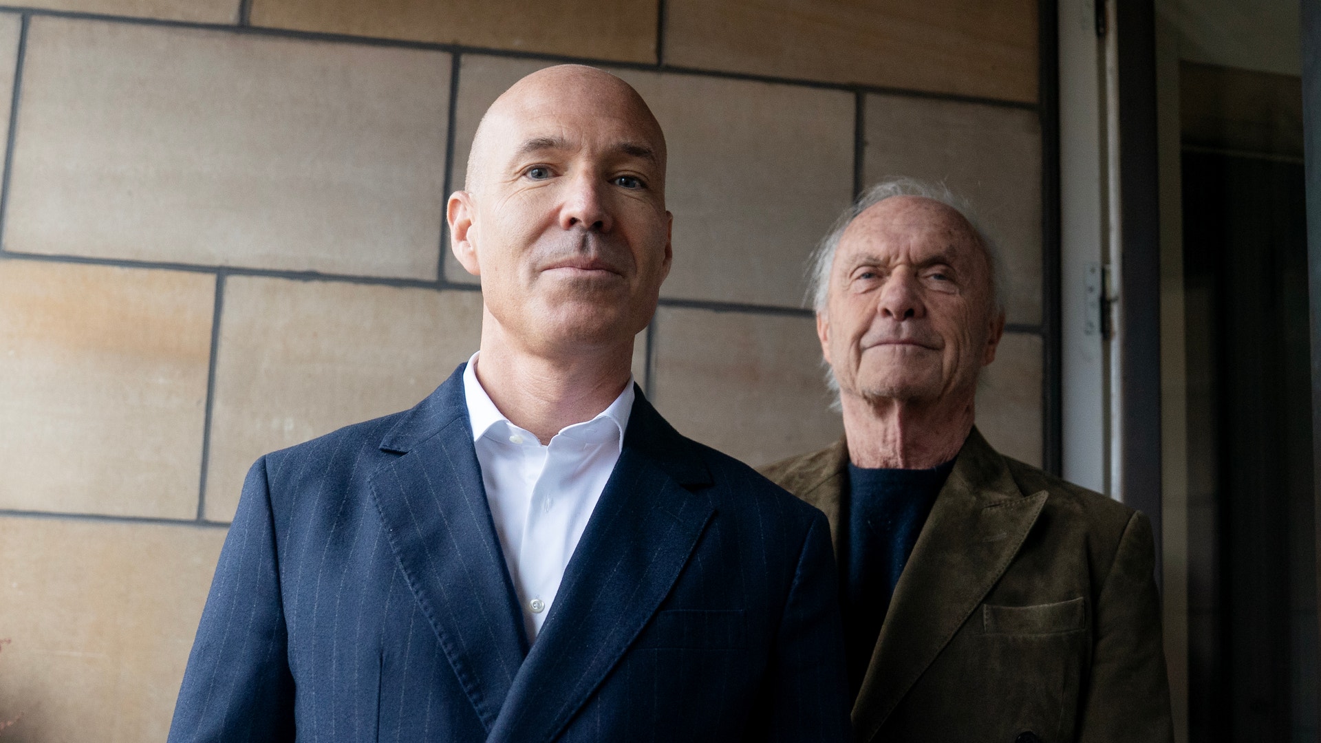 Två män står tillsammans framför en vägg med moderna kakelplattor.