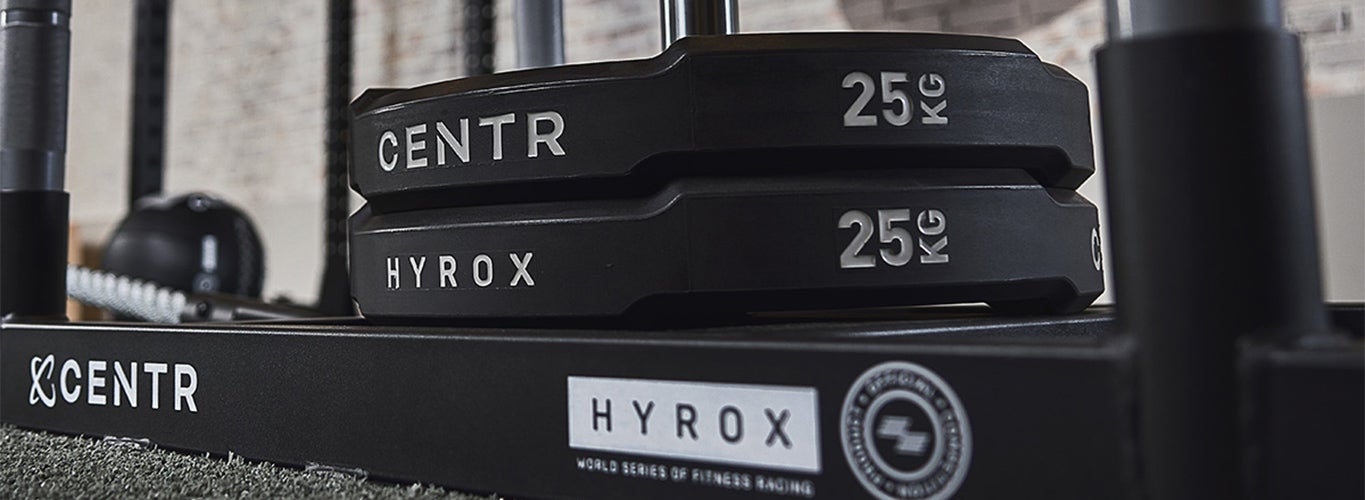 Två svarta viktskivor på 25 kilo staplade på en träningsställning, märkta med Centr och Hyrox.