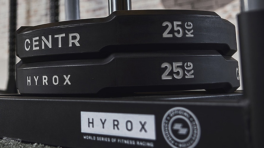 Två svarta viktskivor på 25 kilo staplade på en träningsställning, märkta med Centr och Hyrox.
