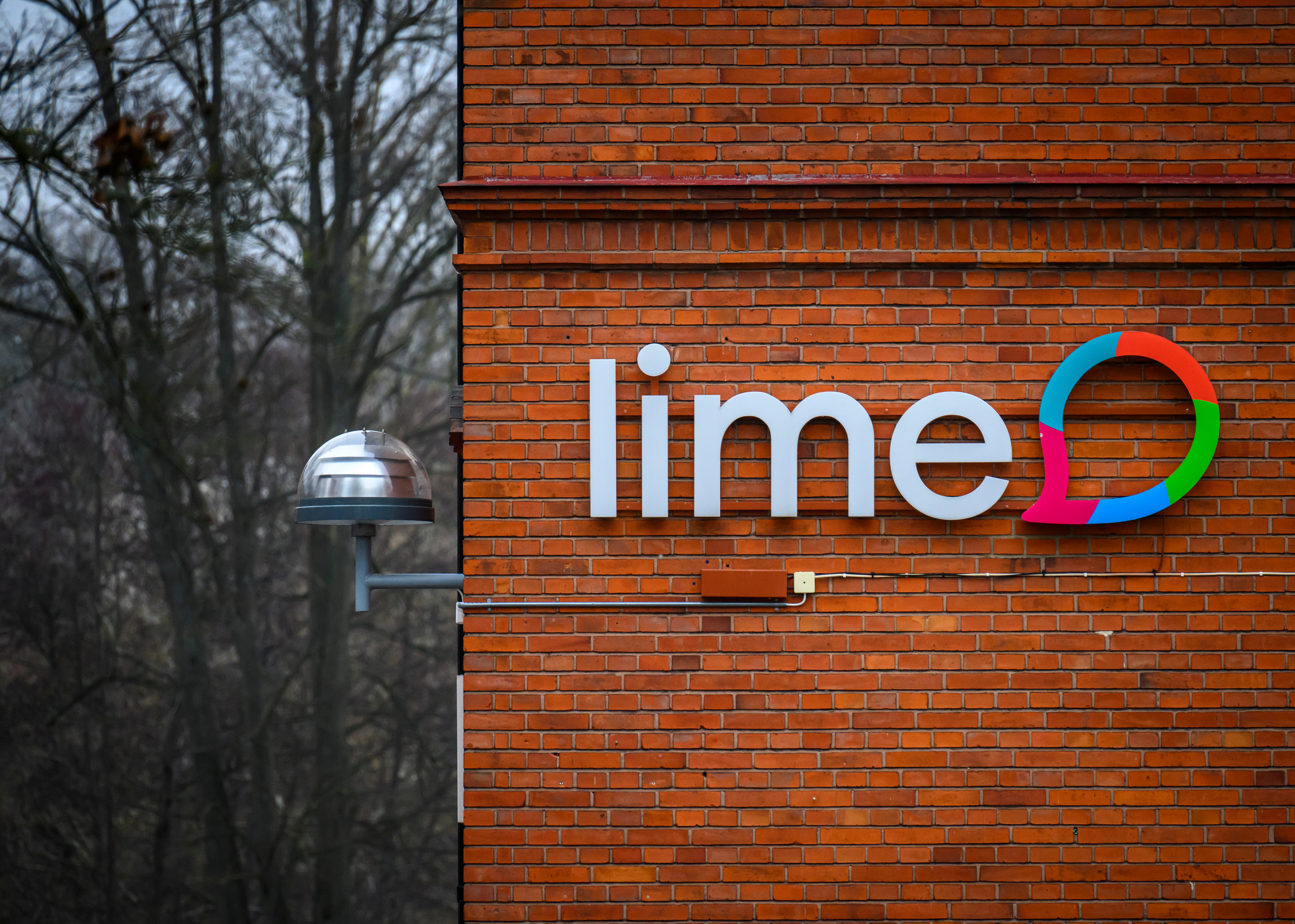 Lime-logotyp på en röd tegelvägg med nakna träd i bakgrunden