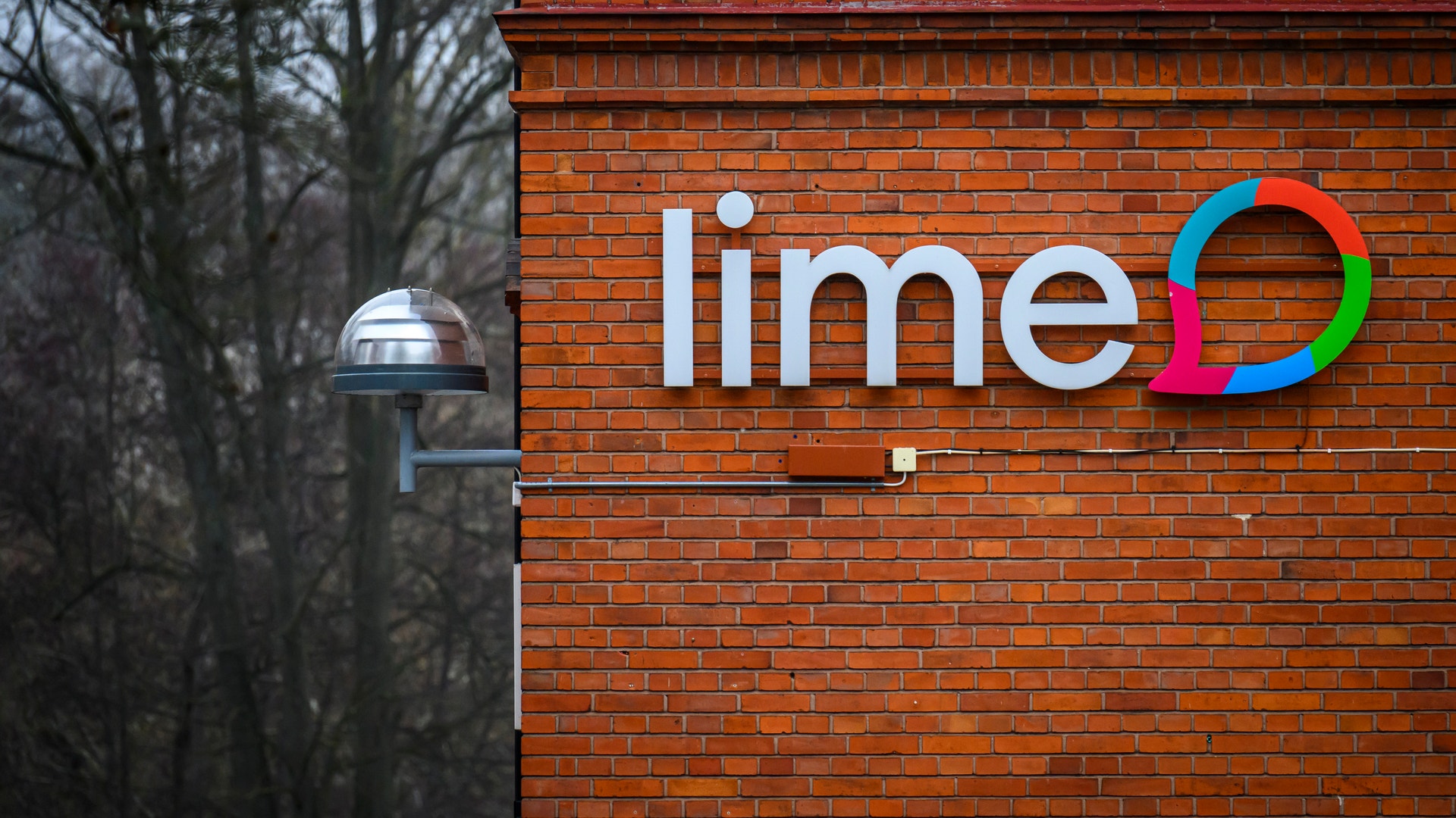 Lime-logotyp på en röd tegelvägg med nakna träd i bakgrunden