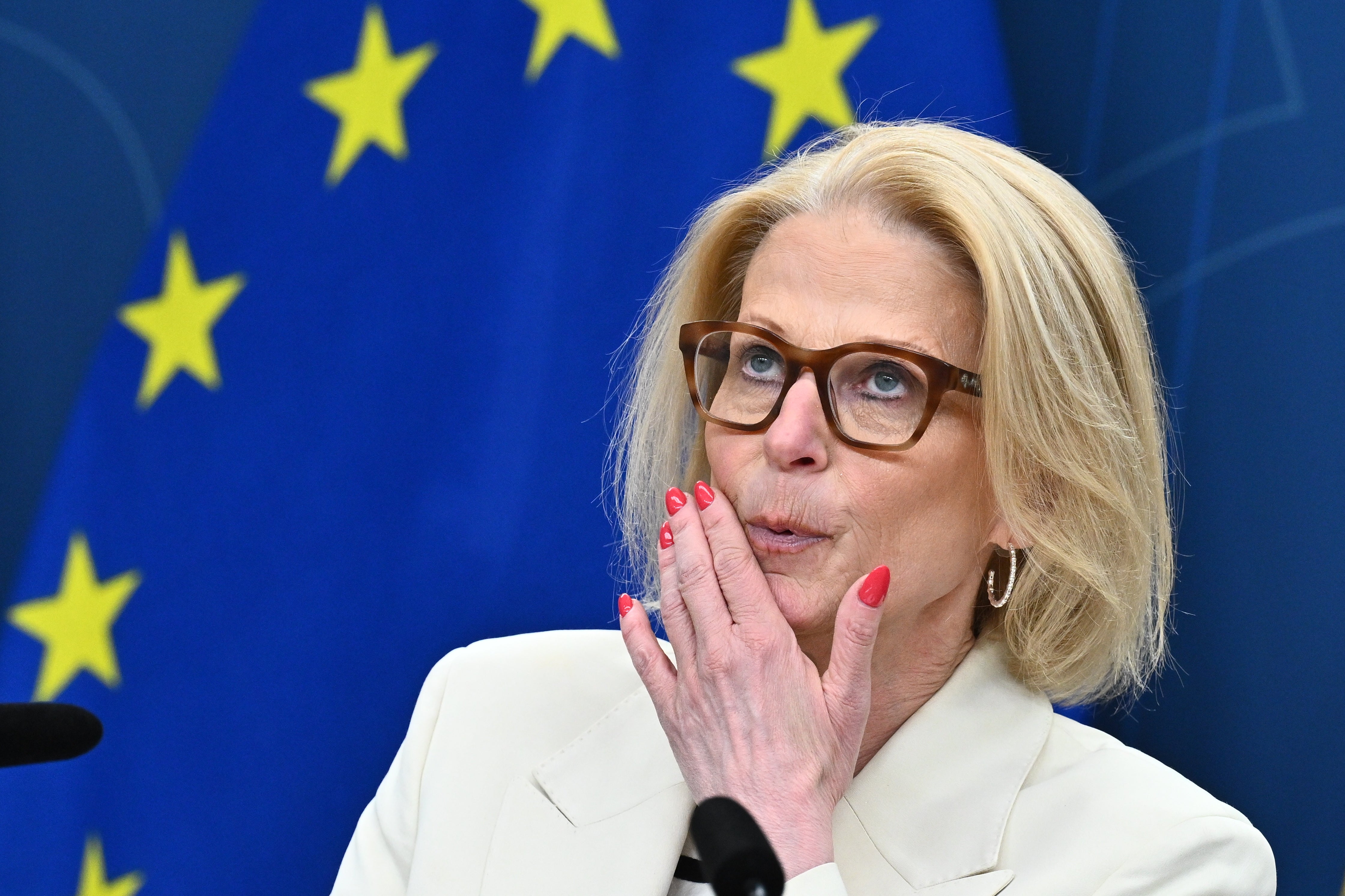Kvinna med glasögon och vit blazer framför EU:s flagga