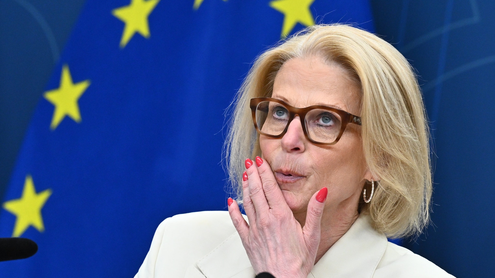 Kvinna med glasögon och vit blazer framför EU:s flagga