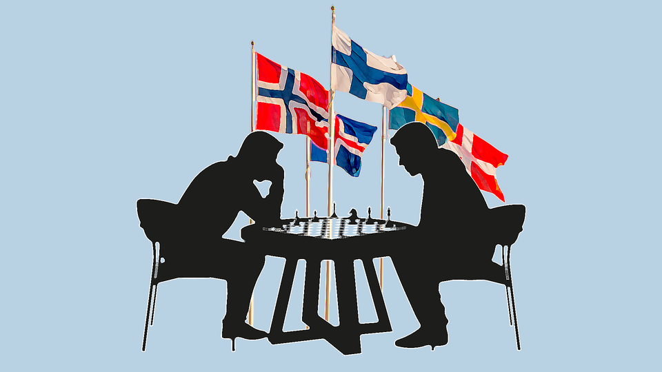 Två personer spelar schack med nordiska flaggor i bakgrunden