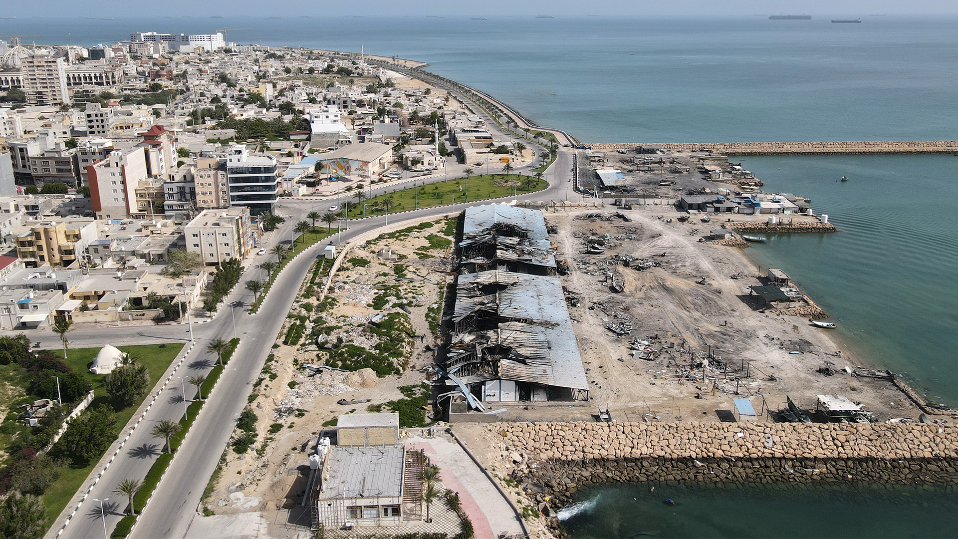 Flygfoto över kuststaden Qeshm med vita byggnader, vägar, hamn och turkosblått vatten.