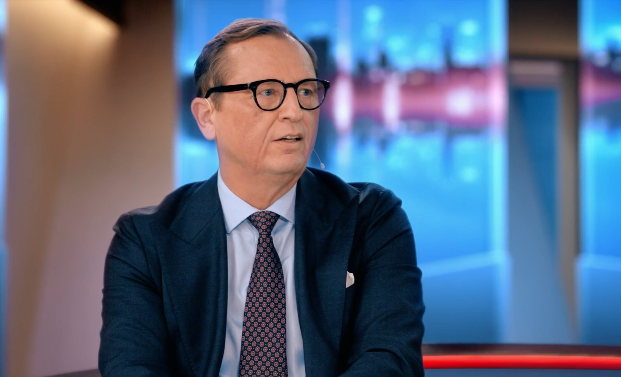 En man i kostym och glasögon sitter i en tv-studio.