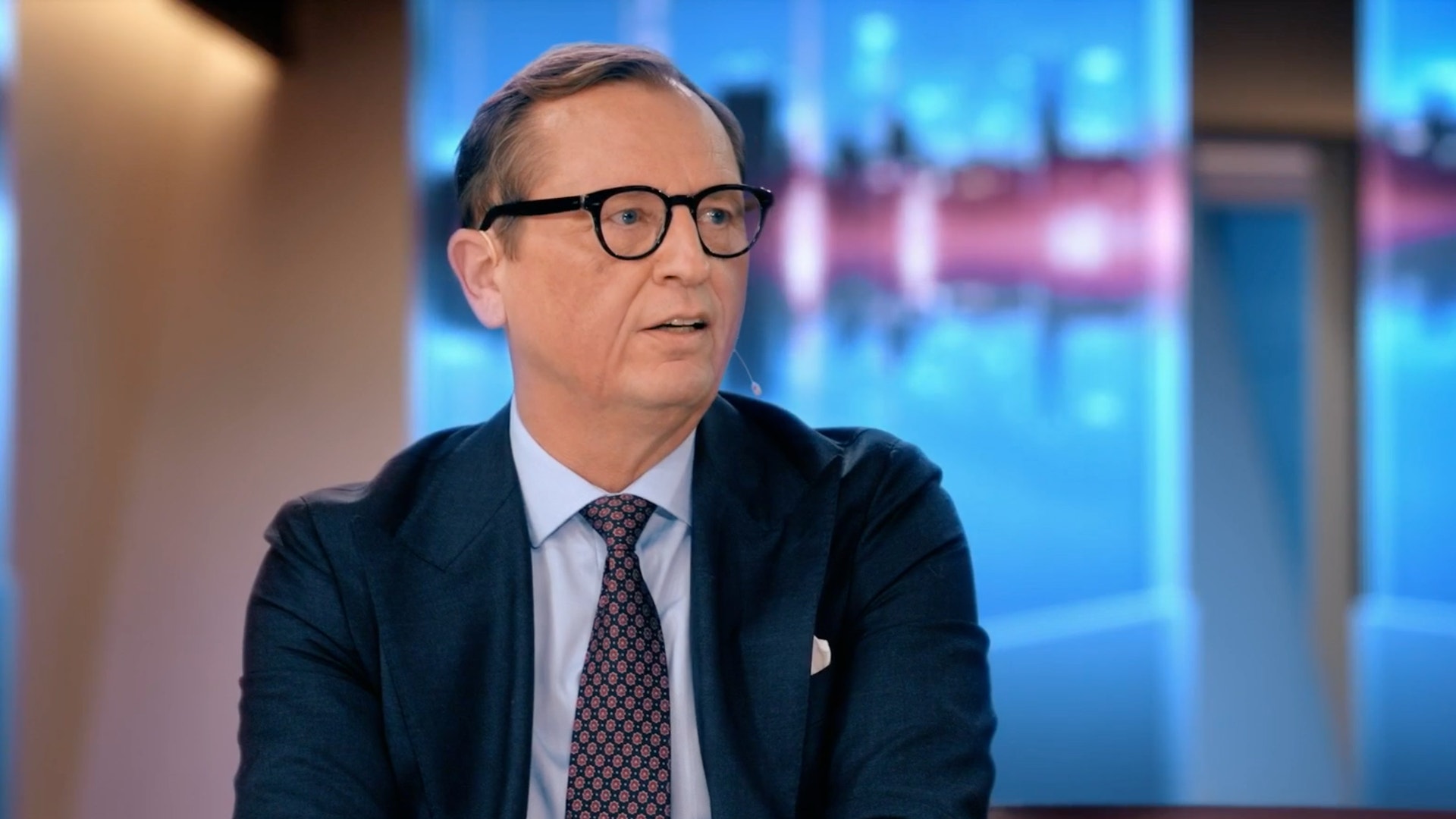 En man i kostym och glasögon sitter i en tv-studio.