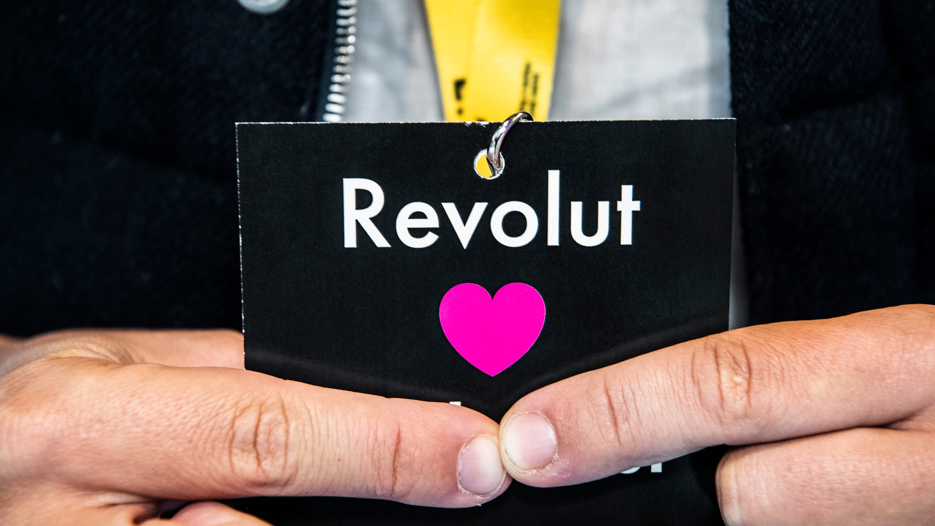 Hand som håller ett svart ID-kort med Revolut-logotypen och ett rosa hjärta