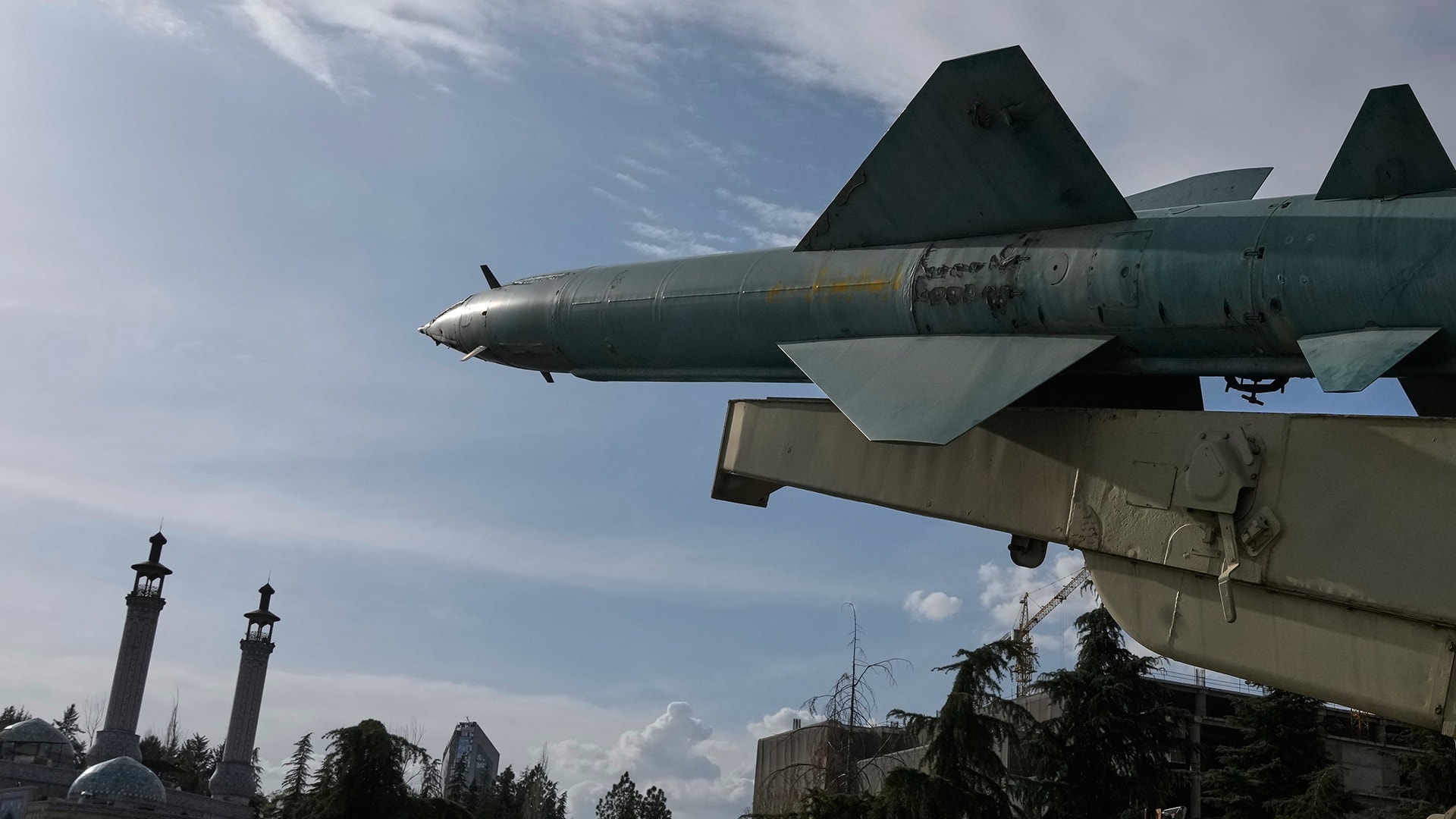 Militärt stridsflygplan monterat som monument mot blå himmel med Teheran i bakgrunden