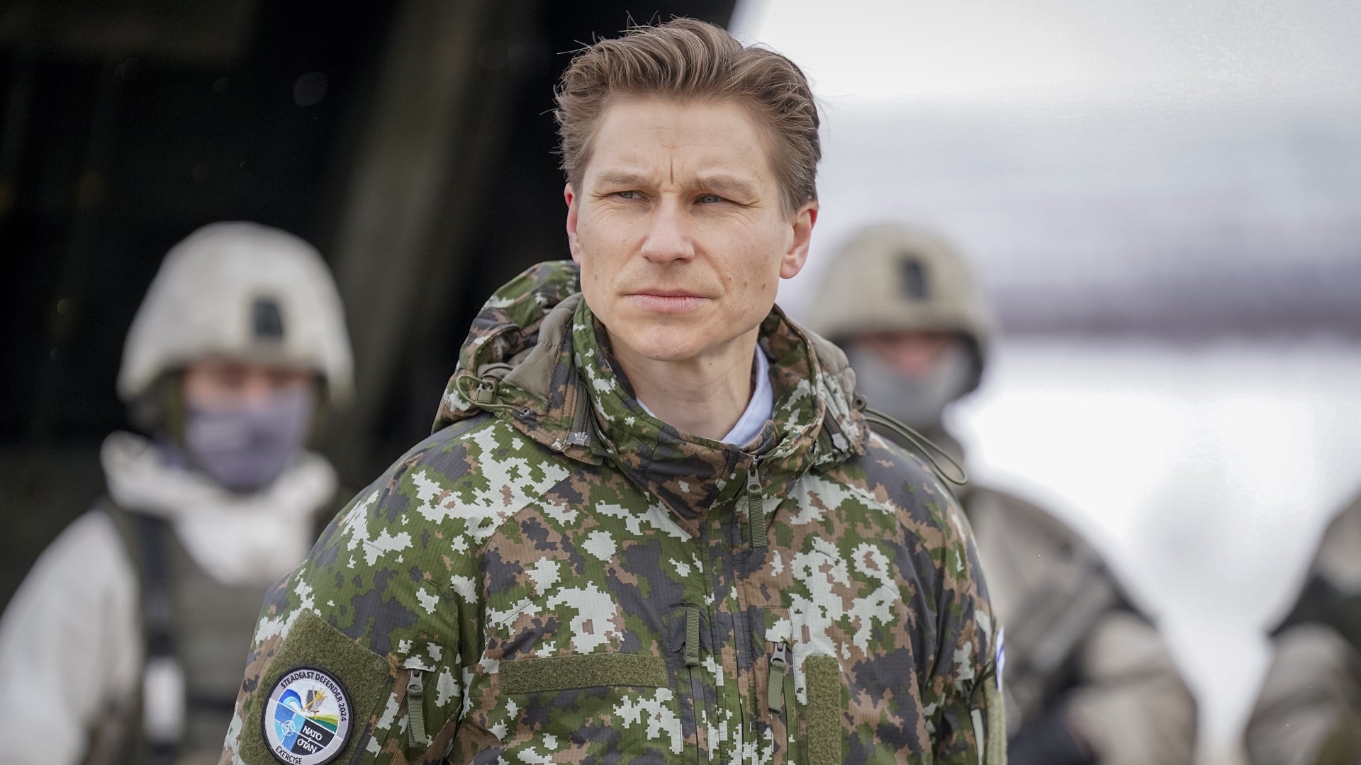 Porträtt av en soldat i kamouflageuniform som tittar mot kameran. Andra soldater syns suddiga i bakgrunden.