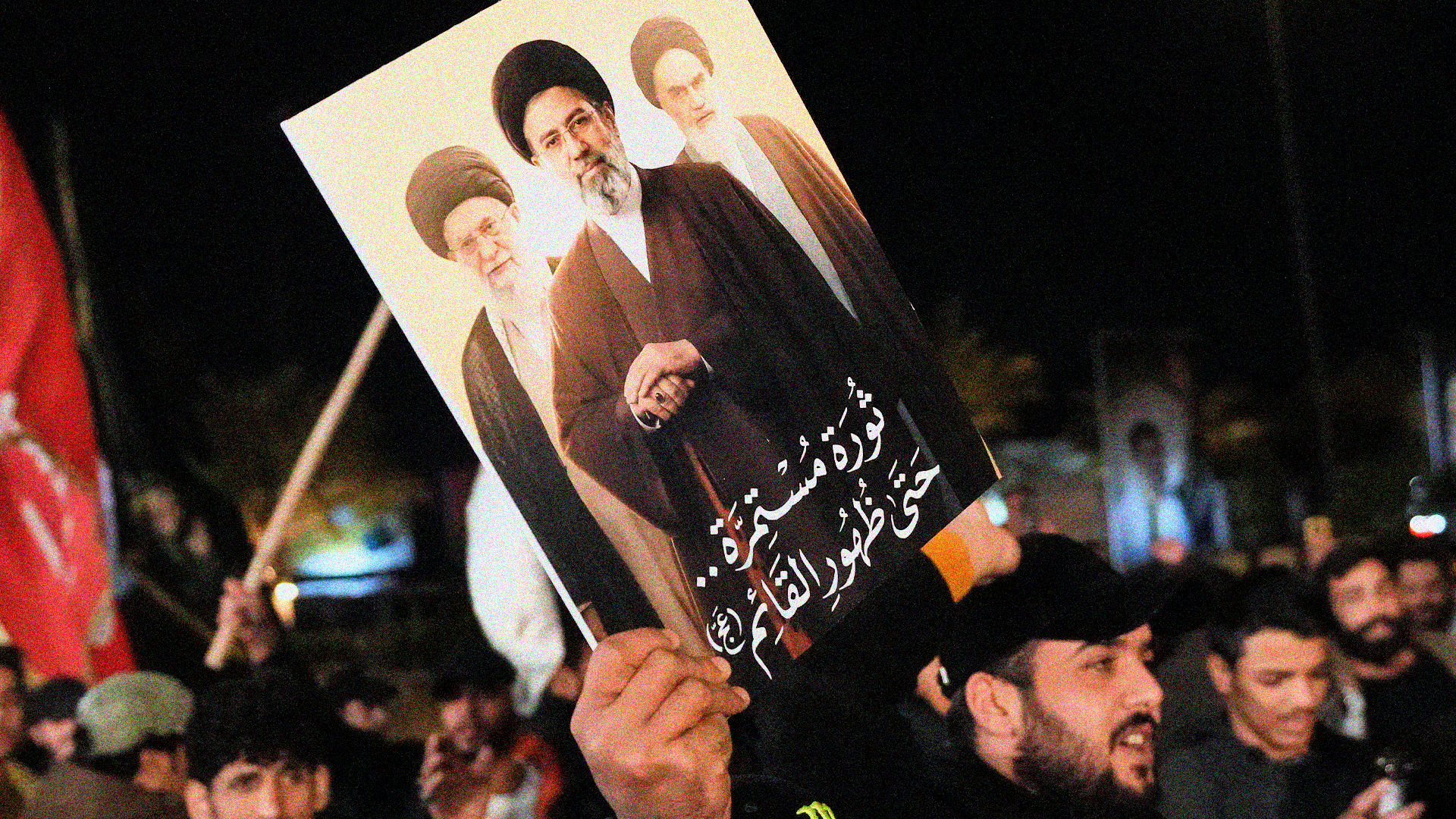 Folksamling där en person håller upp en affisch med porträtt under kvällstid.