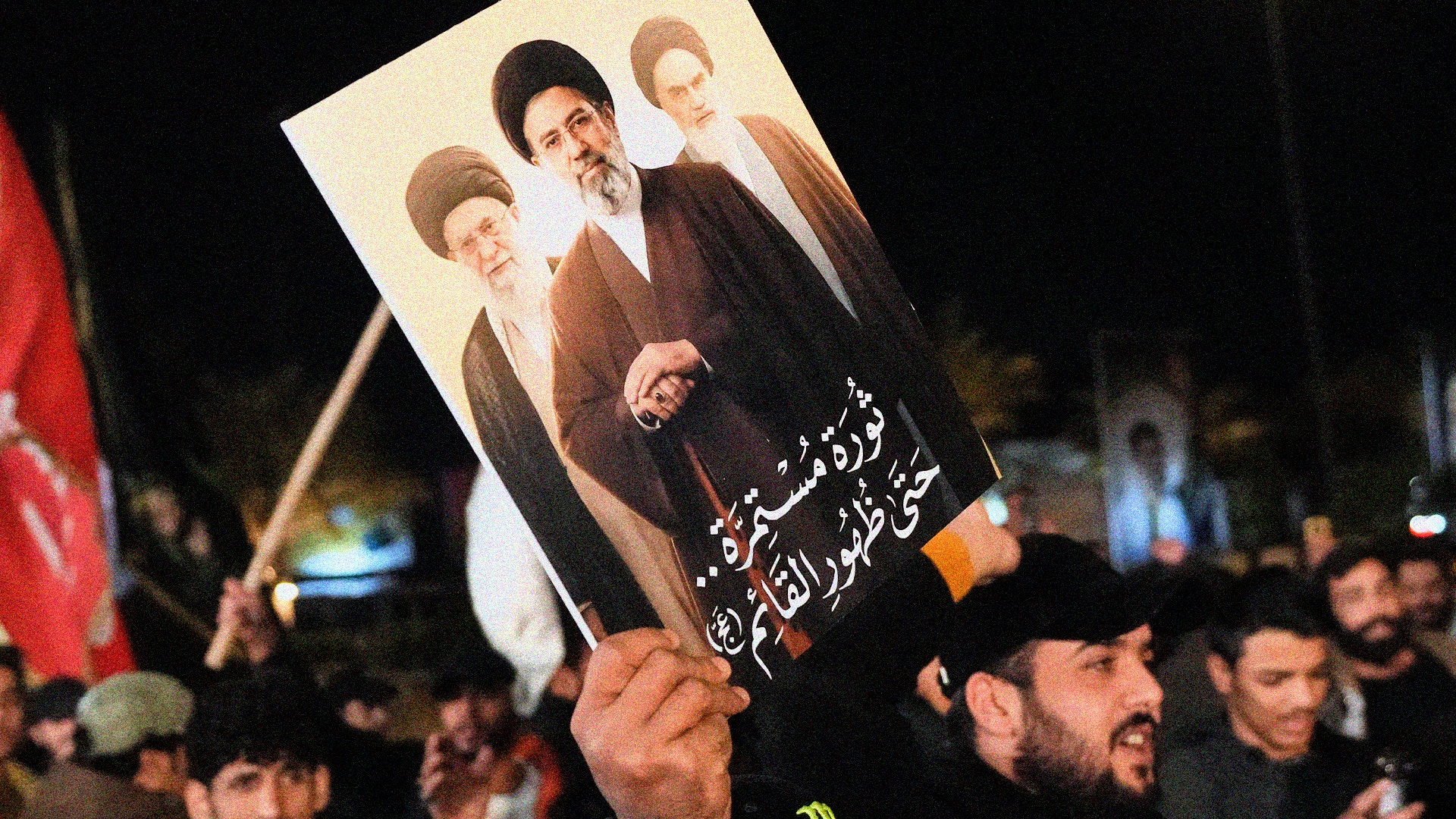 Folksamling där en person håller upp en affisch med porträtt under kvällstid.