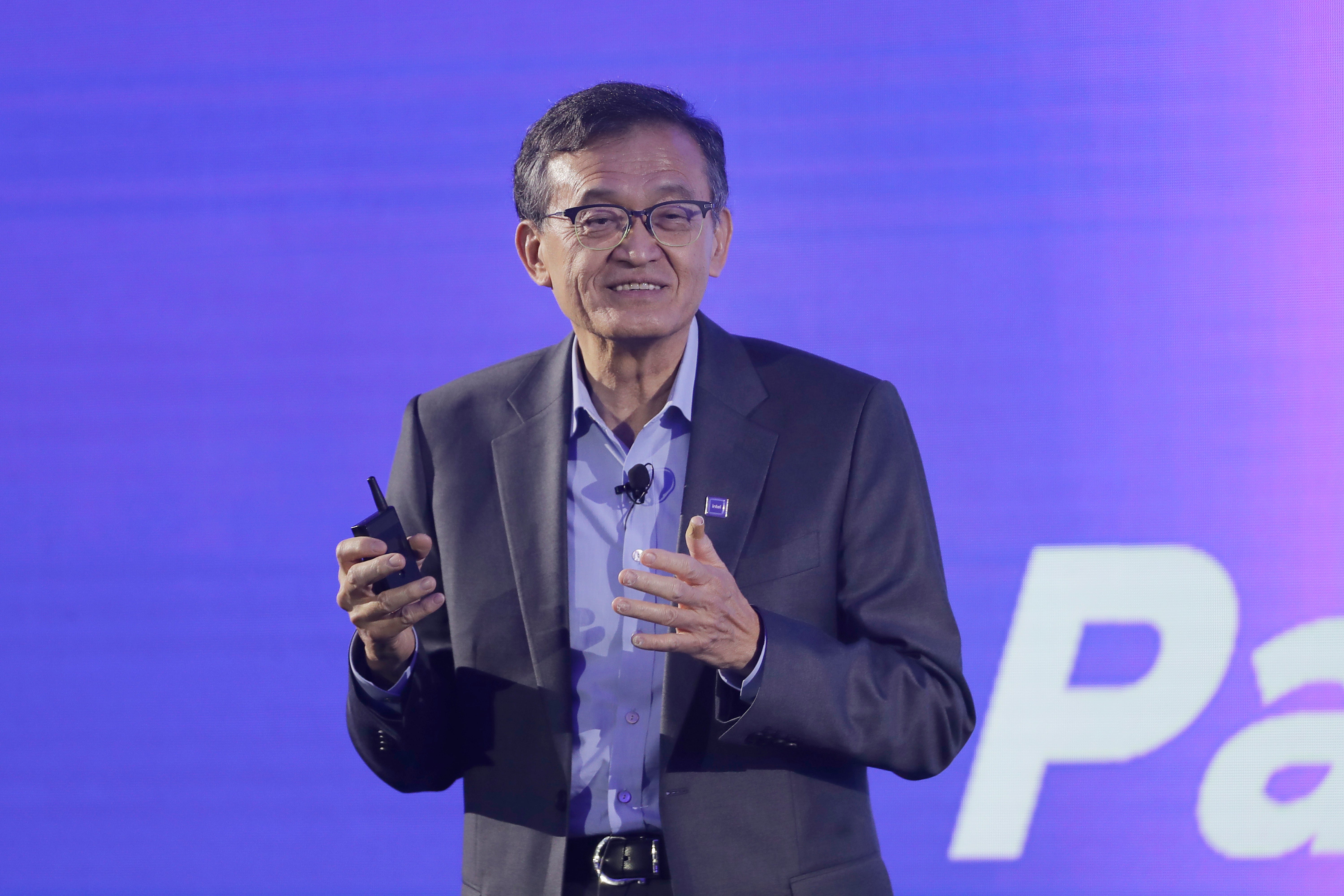 Man i kostym och glasögon som presenterar på scen framför en lila bakgrund.