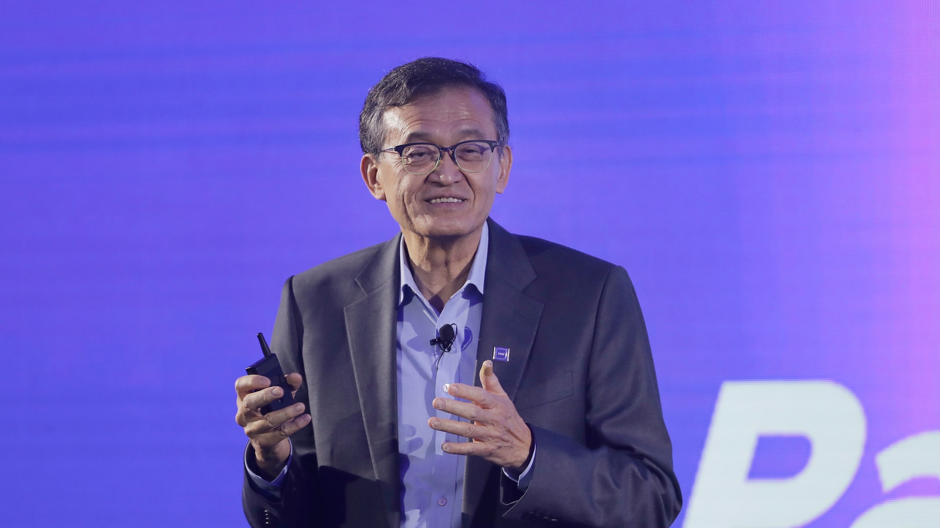 Man i kostym och glasögon som presenterar på scen framför en lila bakgrund.