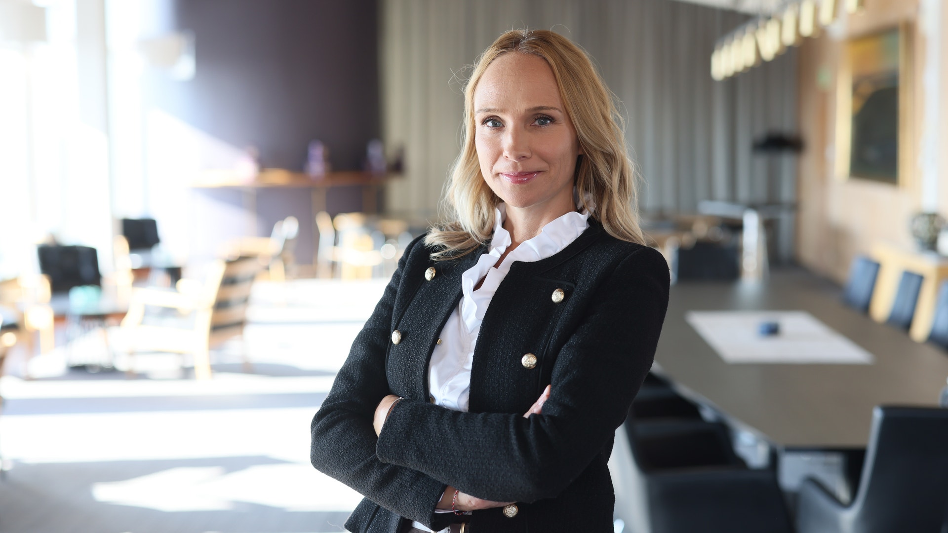 Porträtt av en kvinna i svart kavaj och vit skjorta som står i ett modernt kontorslandskap med armarna i kors.