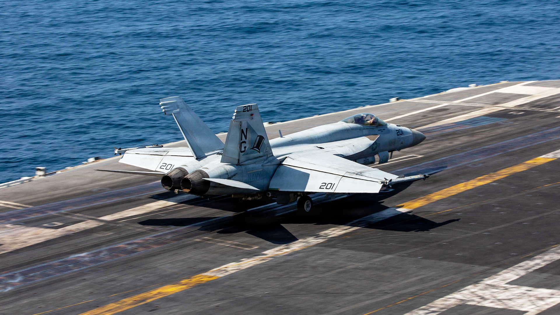 Militärt stridsflygplan på ett hangarskeppsdäck med havet i bakgrunden.