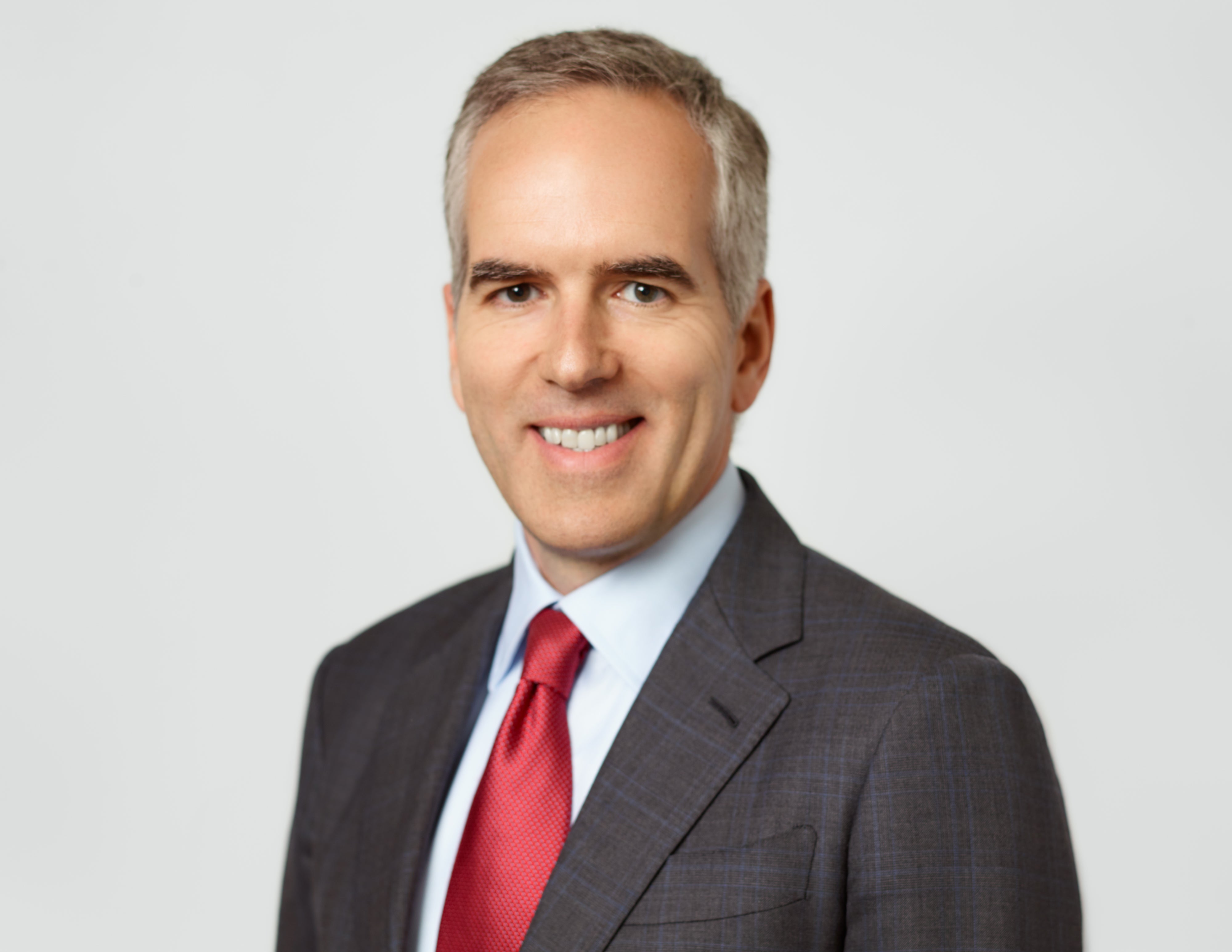 Professionell porträttfoto av en man i mörk kostym och röd slips mot neutral bakgrund.