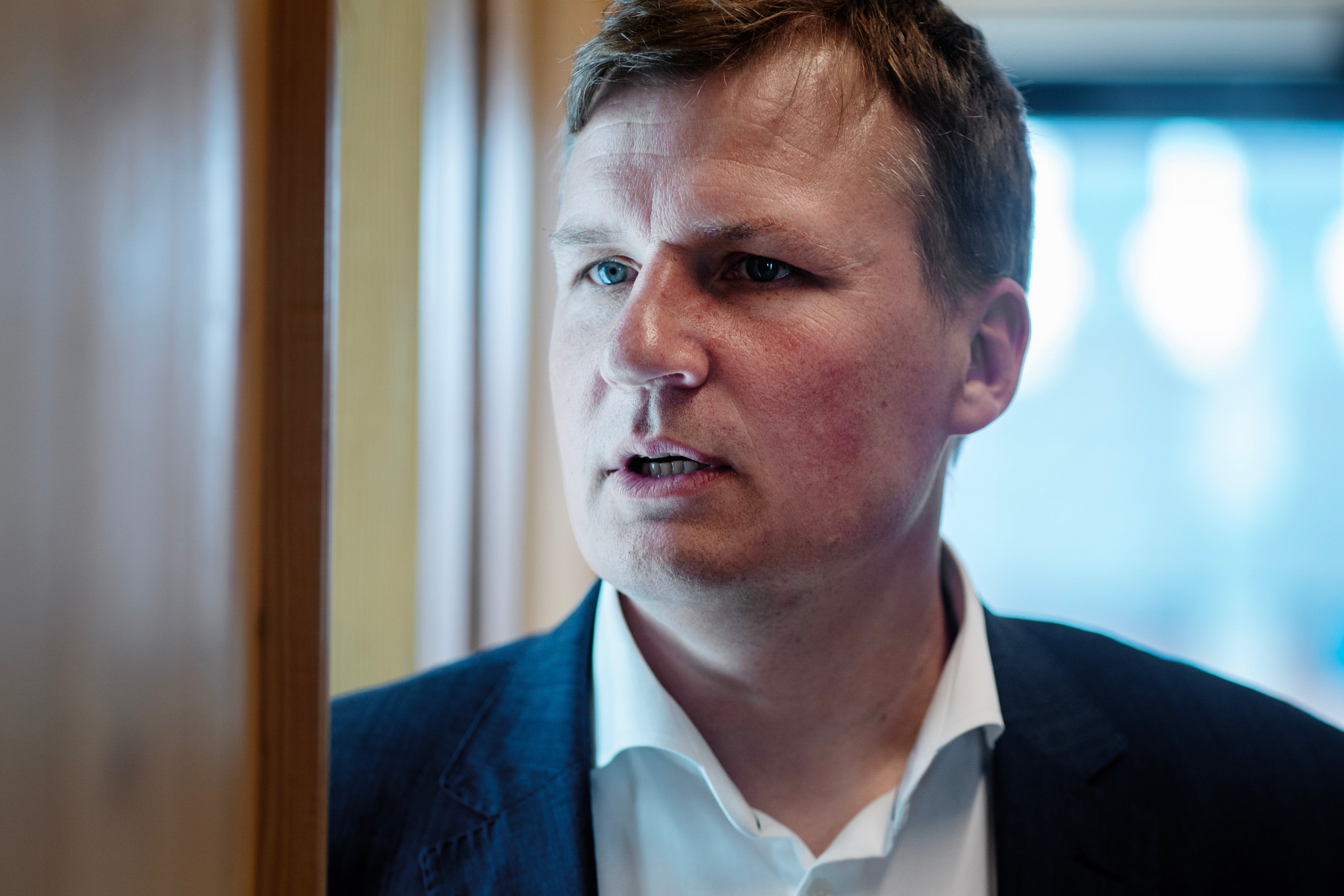 Porträtt av en man i mörk kostym och vit skjorta, fotograferad inomhus.