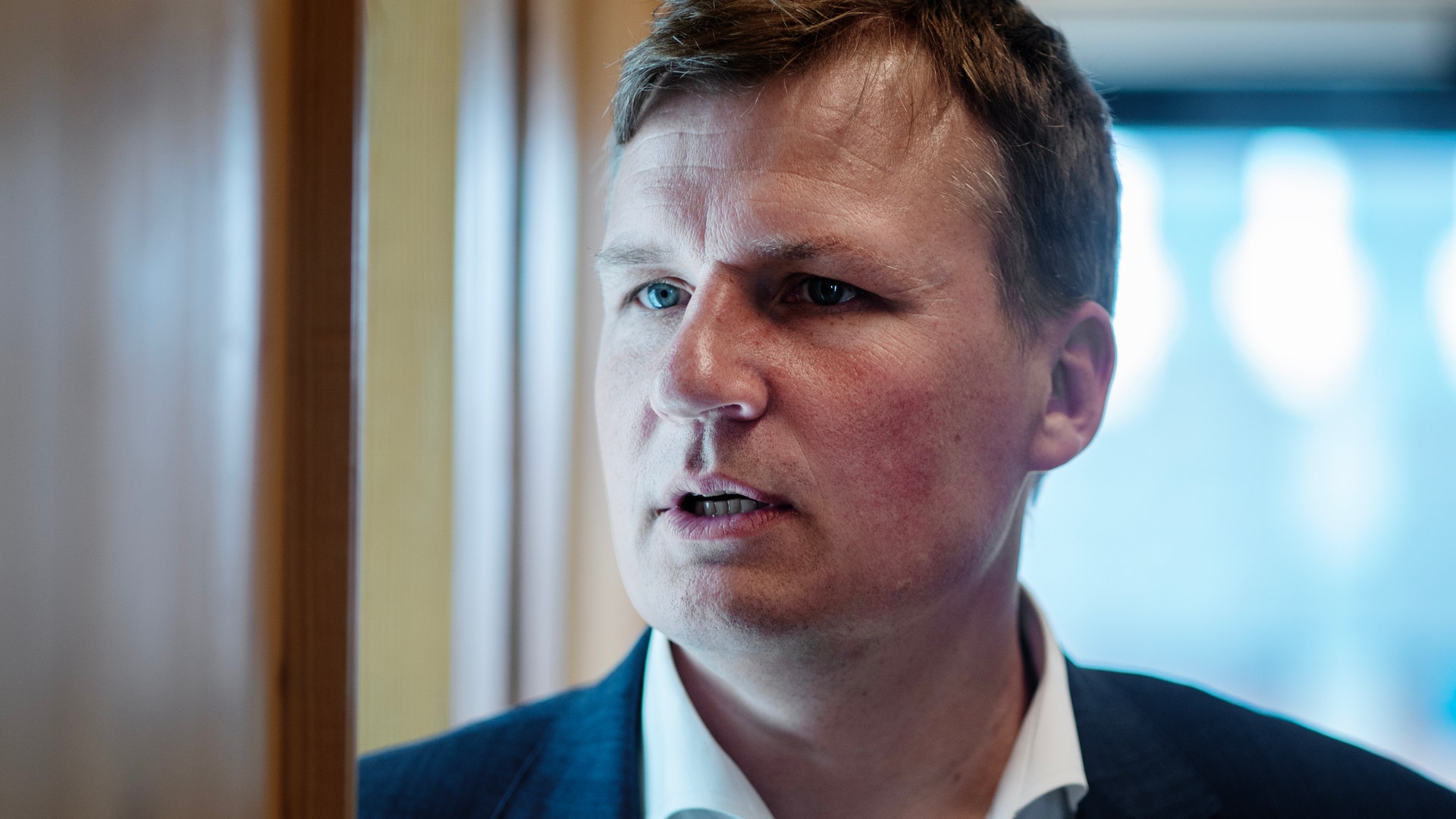 Porträtt av en man i mörk kostym och vit skjorta, fotograferad inomhus.