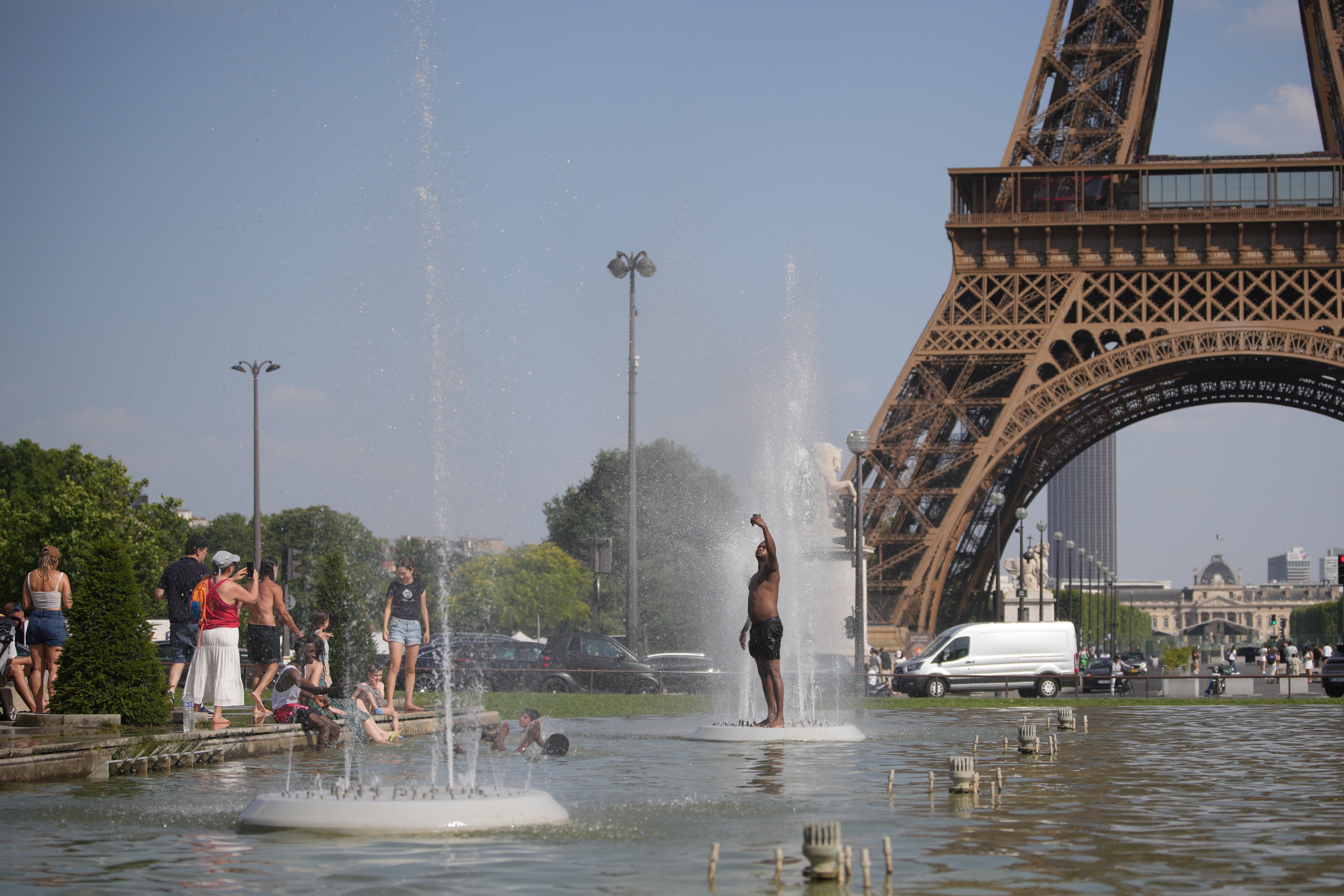 Människor svalkar sig i en fontän under Eiffeltornet i Paris på en solig sommardag.