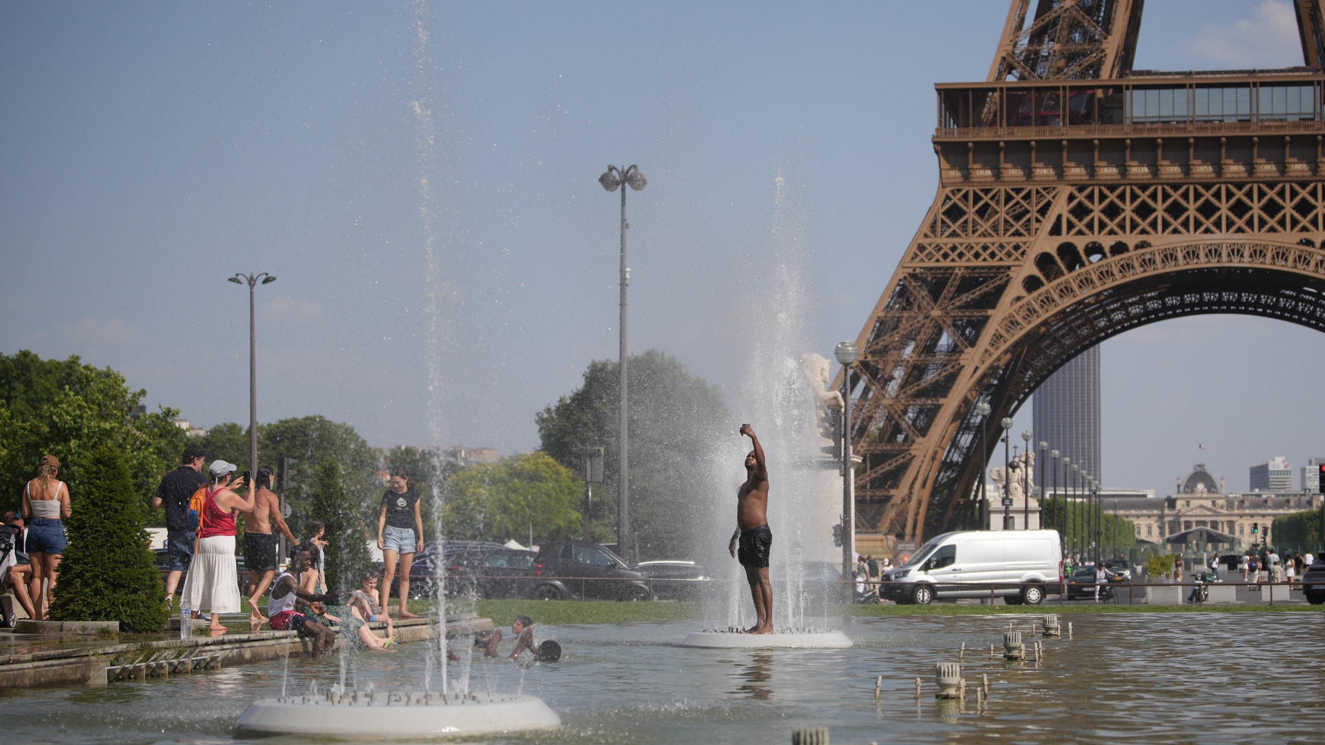 Människor svalkar sig i en fontän under Eiffeltornet i Paris på en solig sommardag.