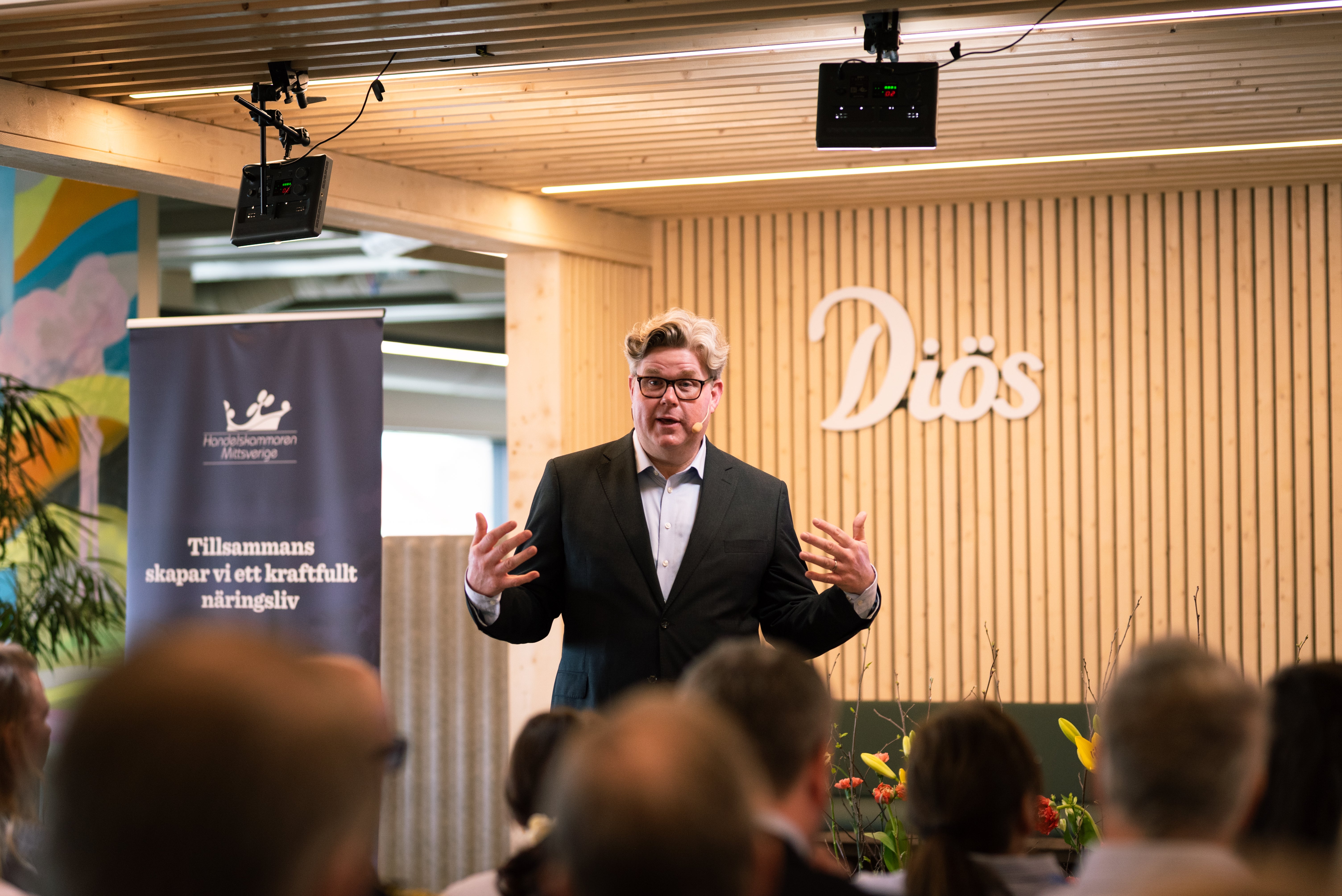 Man i kostym håller ett föredrag framför publik i ett modernt konferensrum