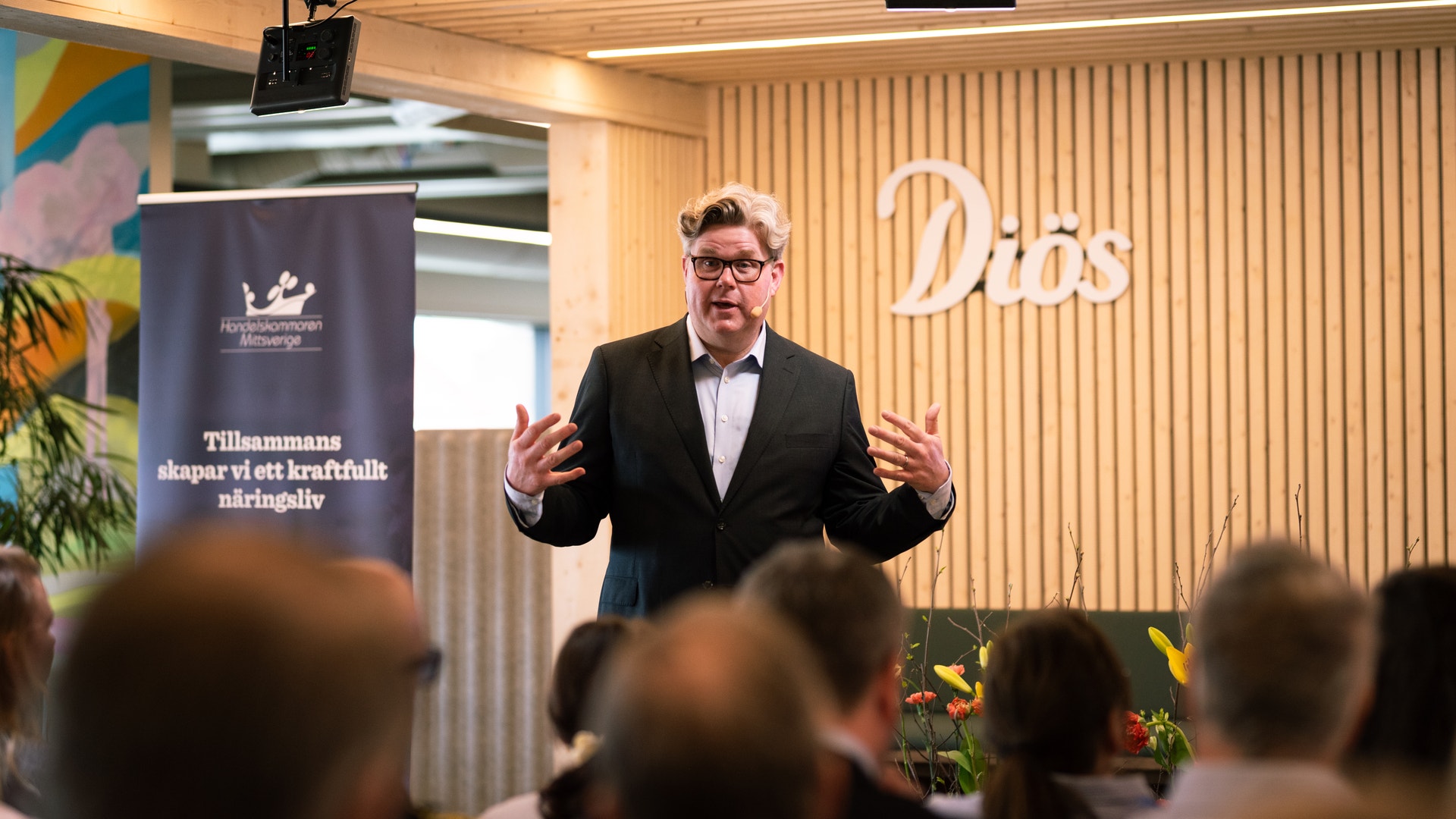 Man i kostym håller ett föredrag framför publik i ett modernt konferensrum