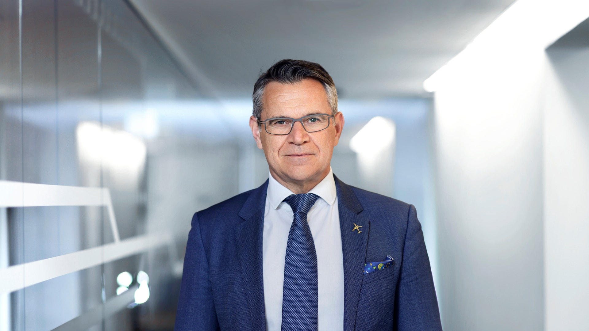 Porträtt av en man i mörkblå kostym och glasögon i en modern kontorsmiljö