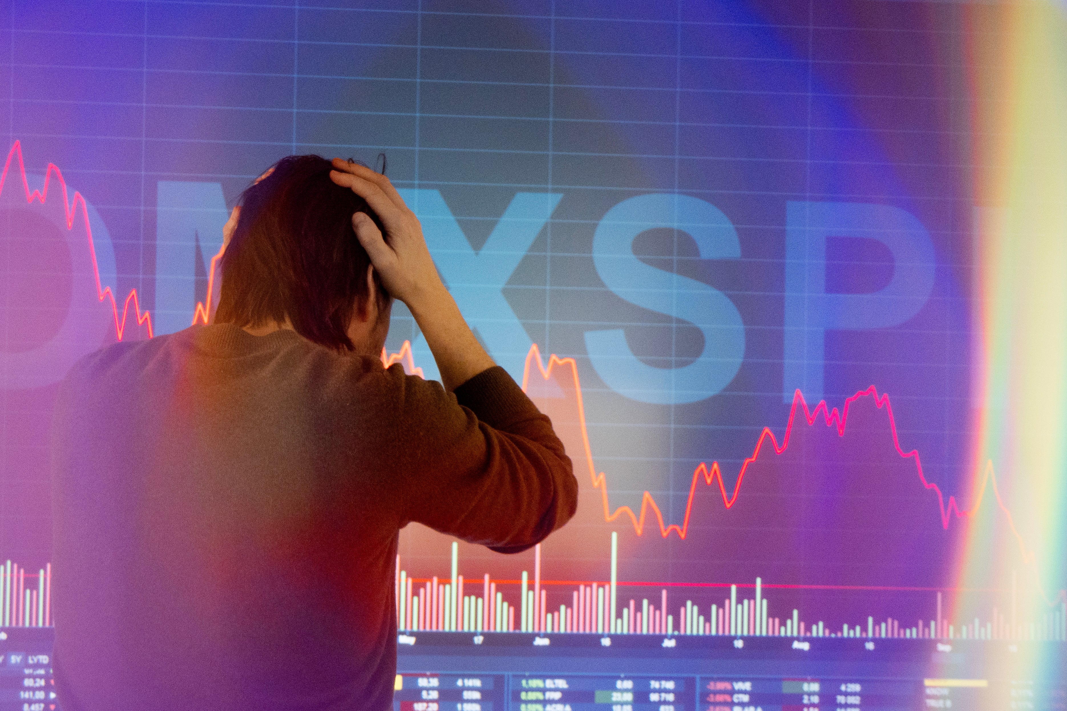 Person som tittar på börskurser med orolig gestalt framför finansiella grafer och marknadsdata.