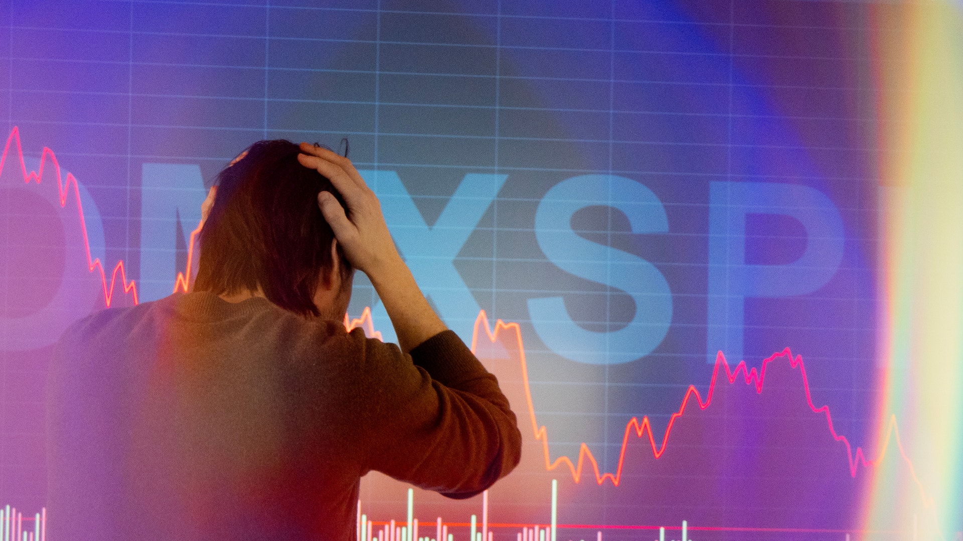 Person som tittar på börskurser med orolig gestalt framför finansiella grafer och marknadsdata.