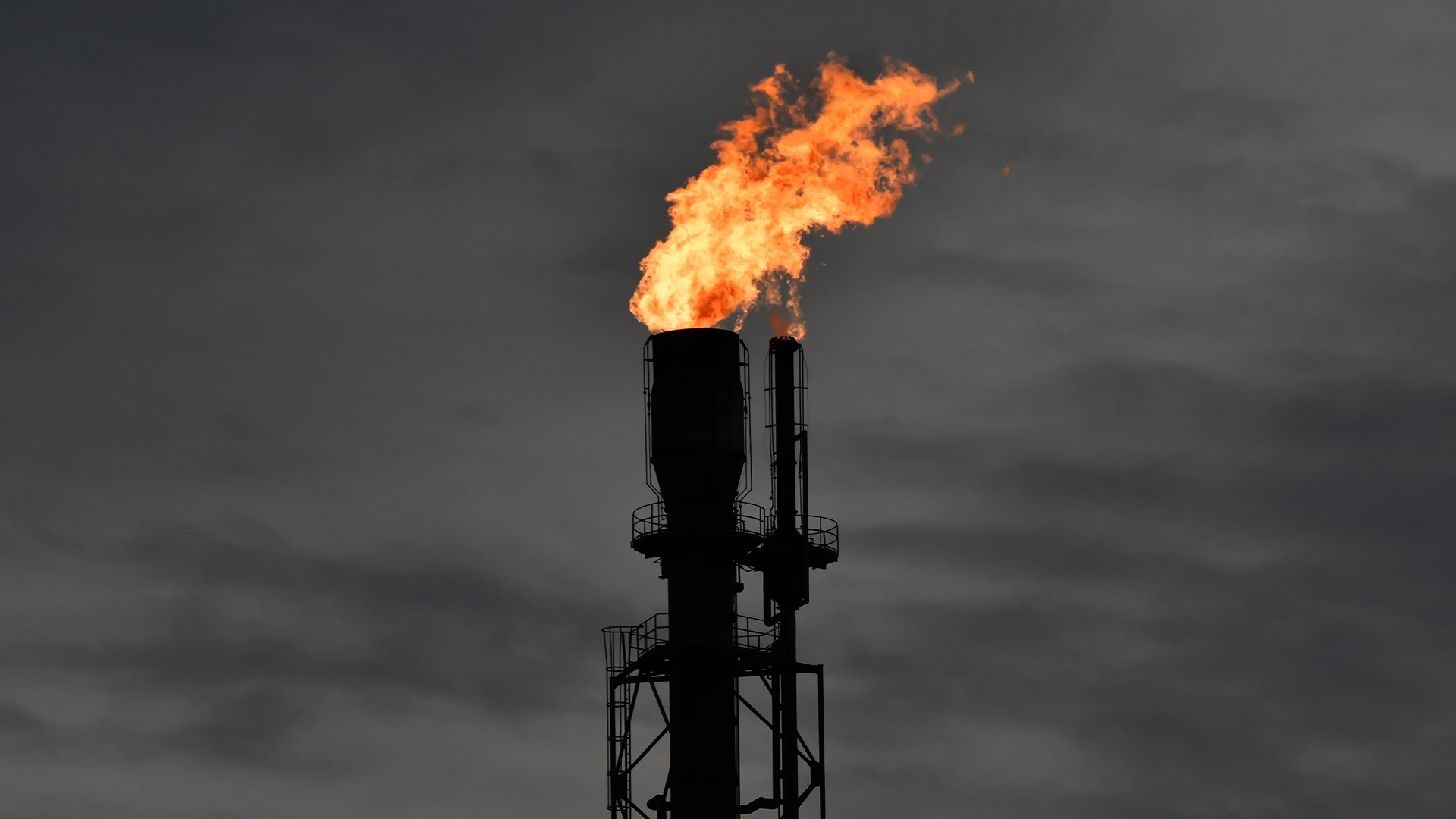 Industriell flörtstack med orange lågor som brinner mot mörk himmel