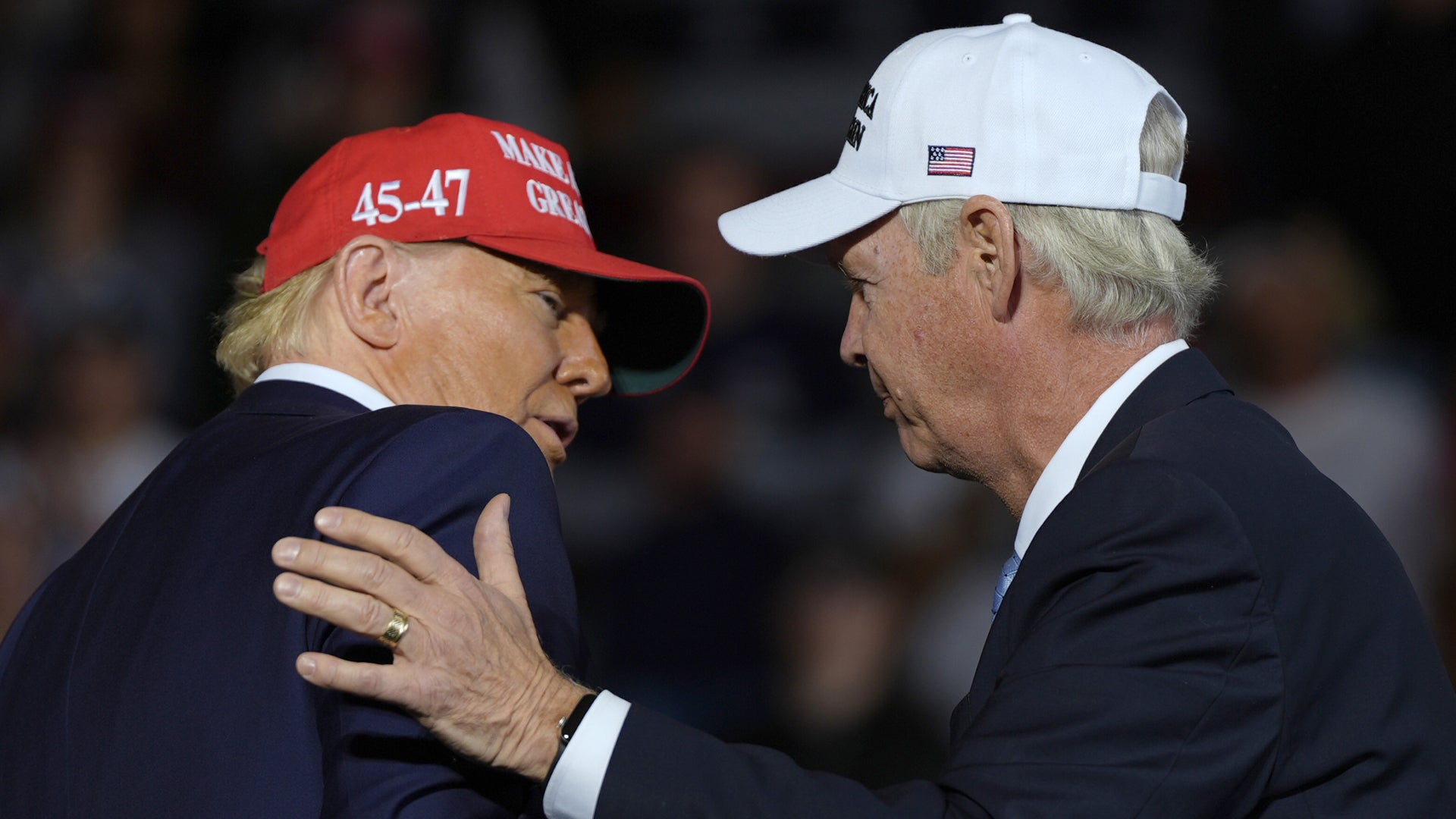 Två män i formell klädsel möts och hälsar på varandra vid ett offentligt event.