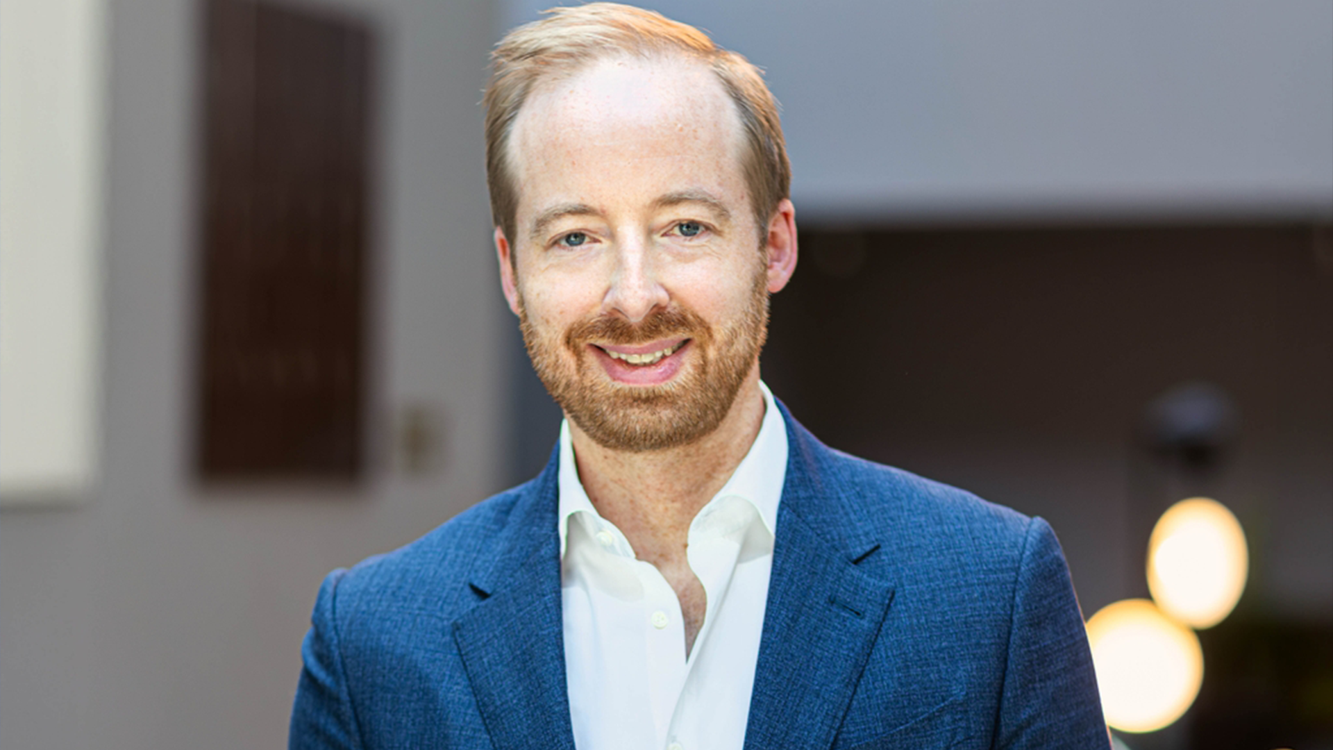 Porträtt av en man i blå kavaj och vit skjorta mot en neutral bakgrund