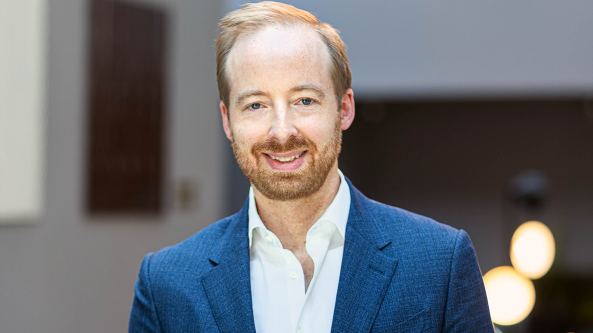 Porträtt av en man i blå kavaj och vit skjorta mot en neutral bakgrund