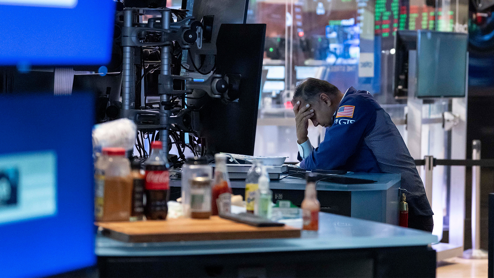 En person i blå skjorta sitter vid ett skrivbord i en TV-studio och håller sitt huvud med handen.