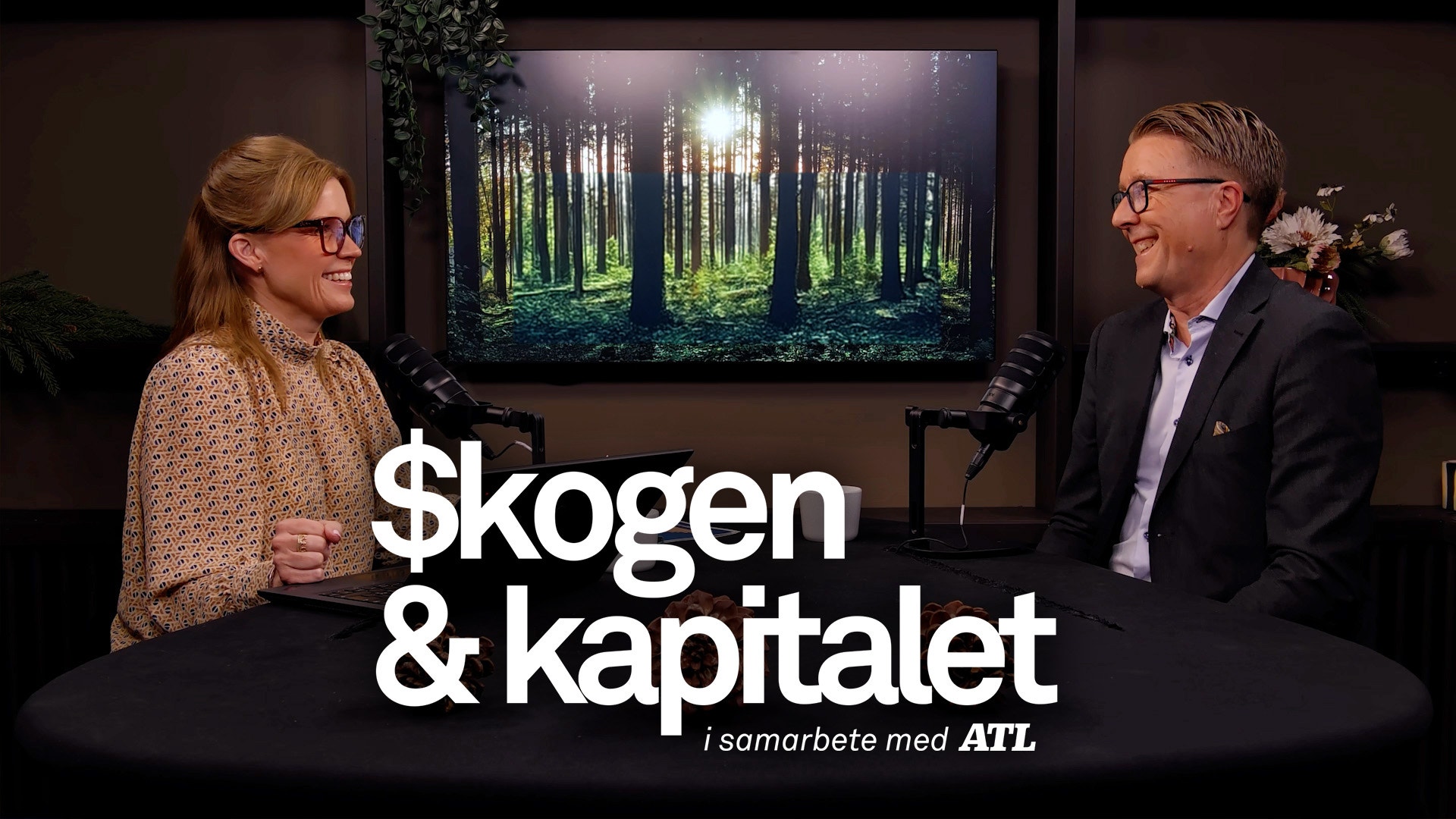 En man och en kvinna sitter och samtalar framför en TV-skärm som visar en skogsmiljö. Texten "$kogen & kapitalet" syns i förgrunden.