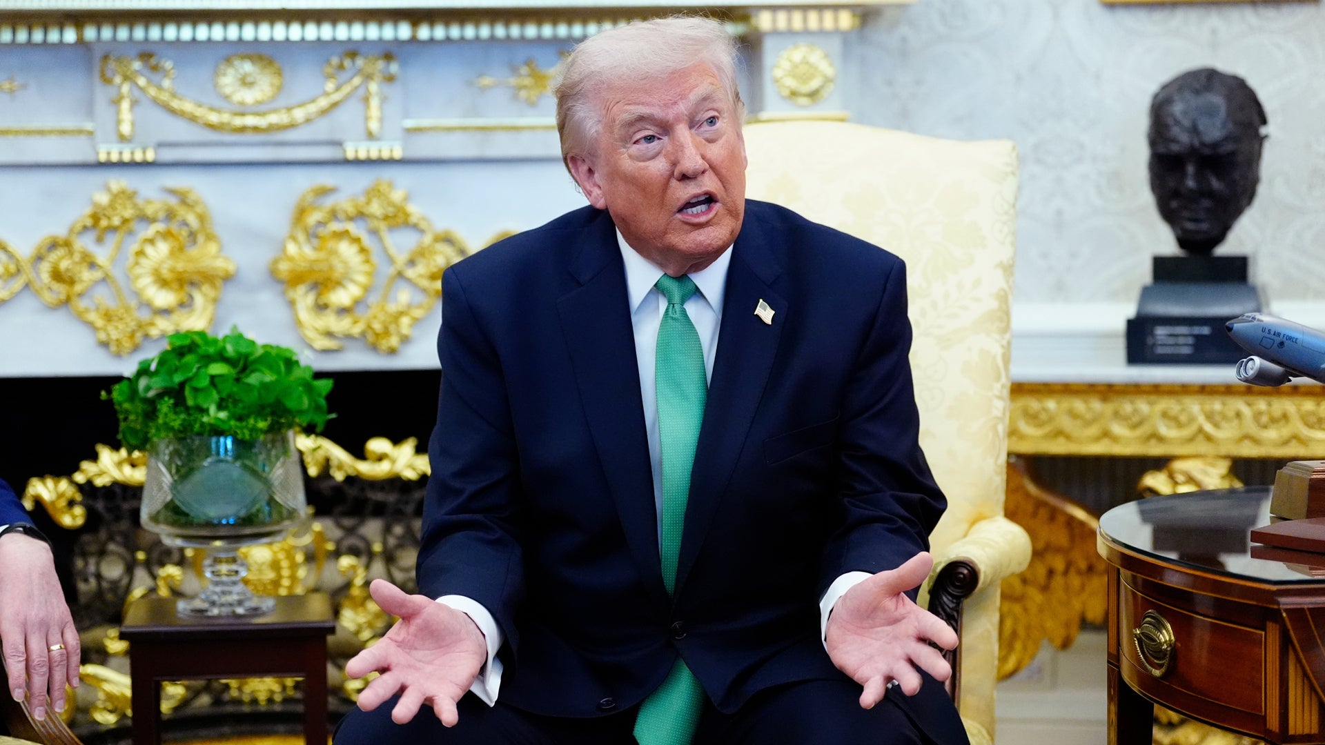 Man i mörk kostym och grön slips sitter i ett elegant kontor med gyllene dekorationer.