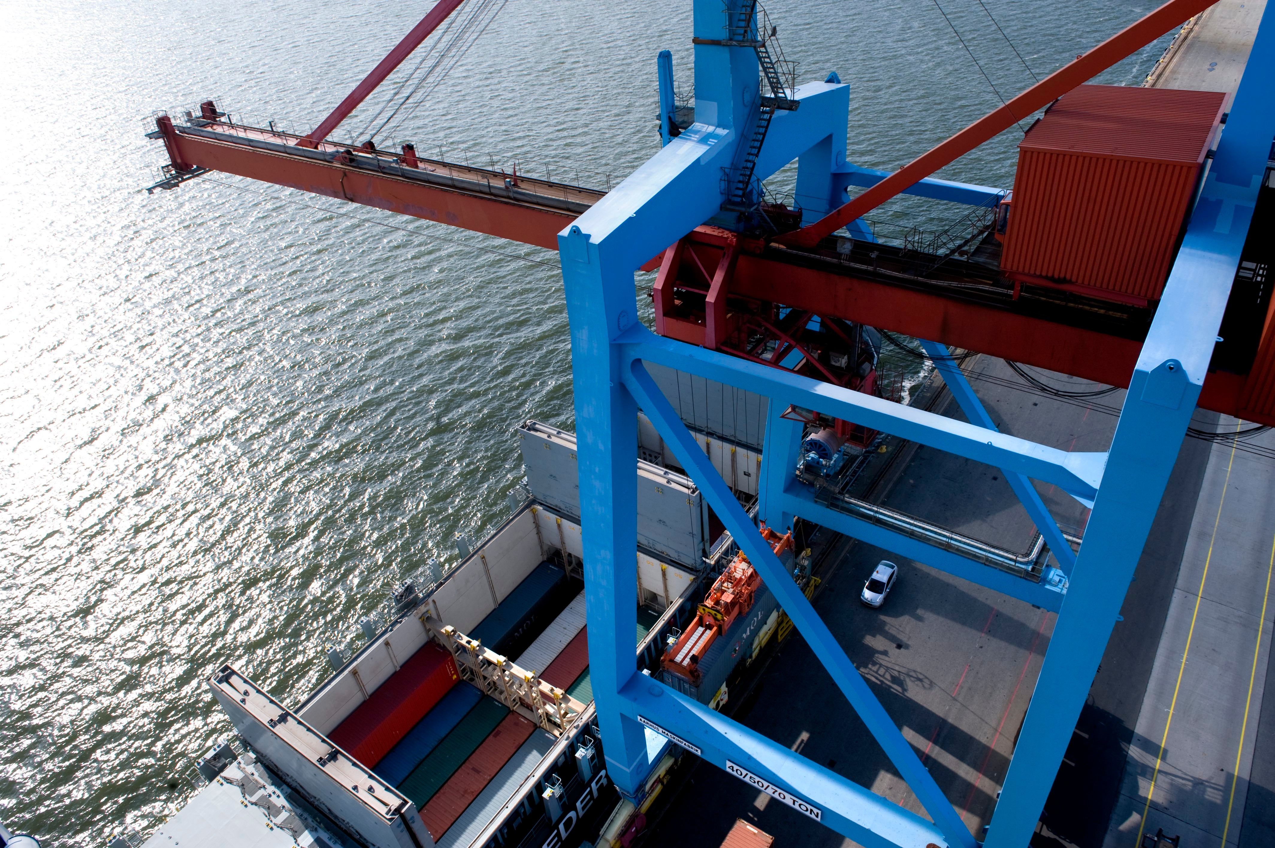 Containerfartyg vid hamn med lastningsekipment och röda och blå kranar för lastning och lossning av frakt.