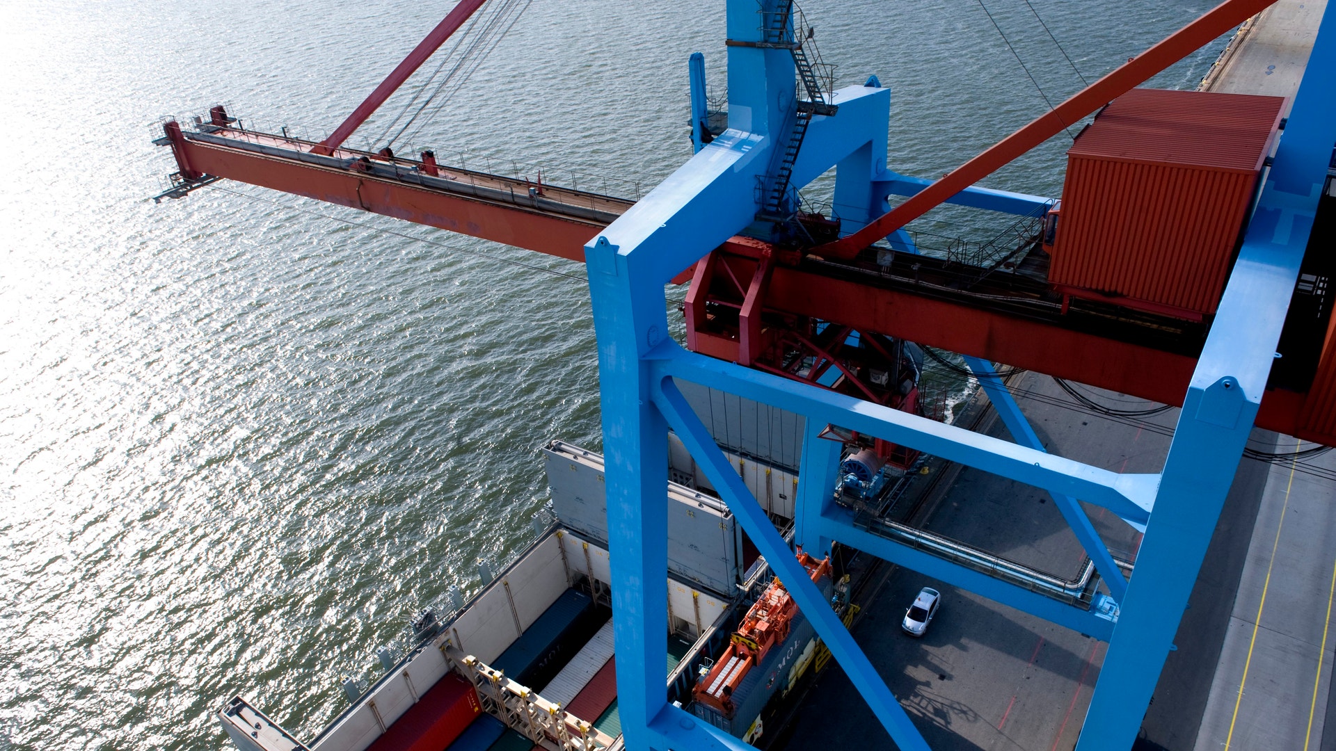 Containerfartyg vid hamn med lastningsekipment och röda och blå kranar för lastning och lossning av frakt.