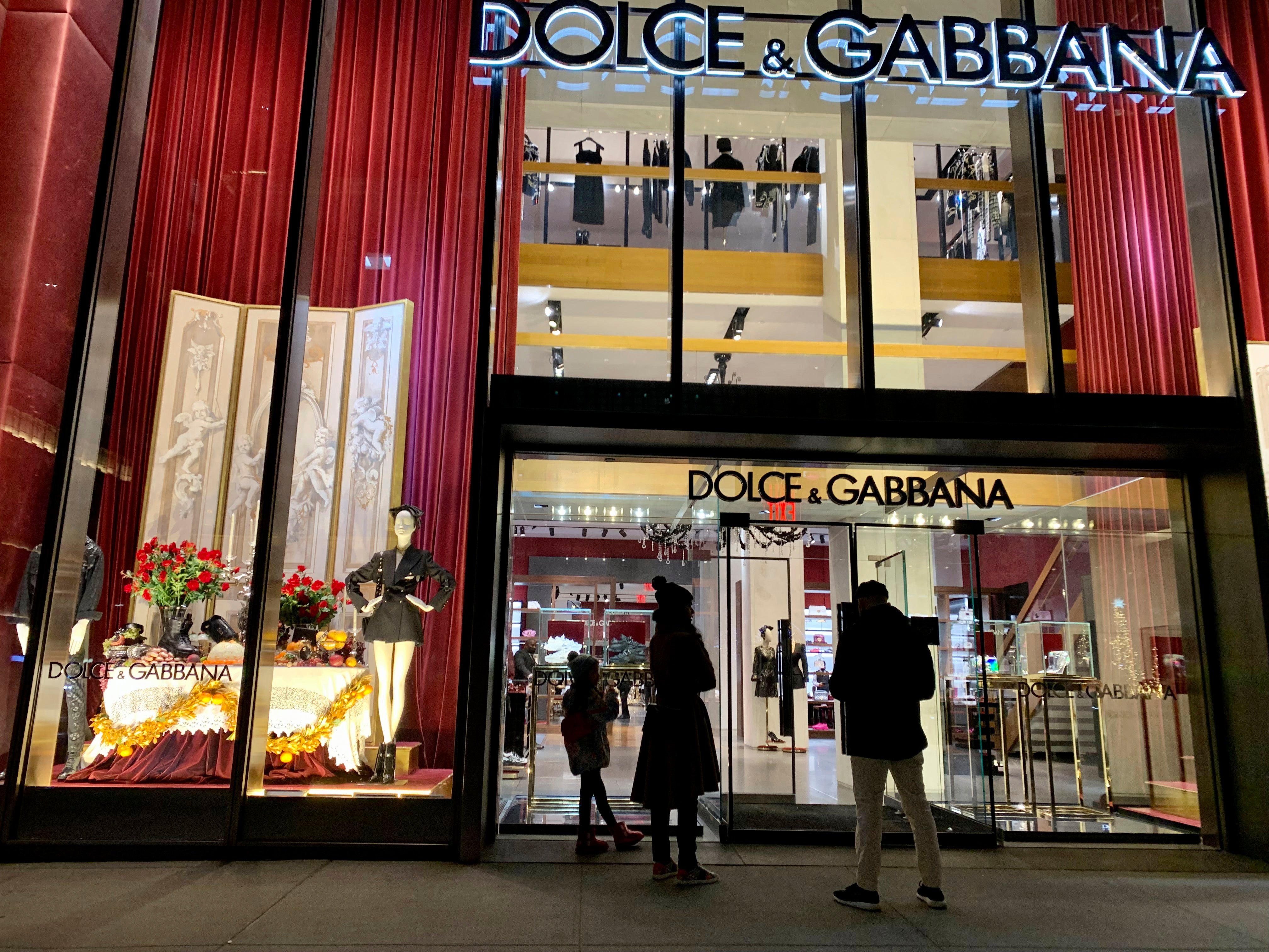 Butiksfasad för Dolce & Gabbana med röda vertikala lameller, stora skyltfönster och människor som går förbi på gatan.